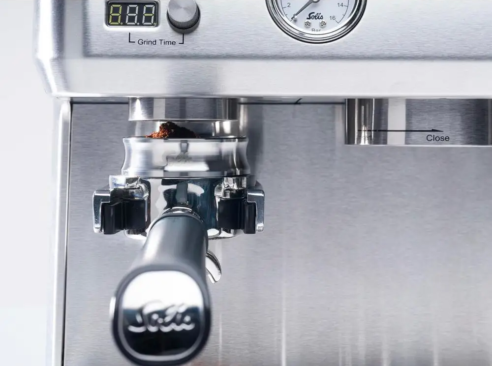 Dettaglio macchina per caffè con portafiltro con caffè macinato e manometro.