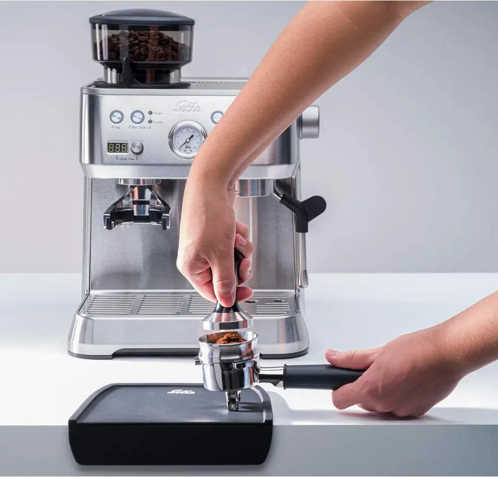 Una persona che pressa la polvere di caffè in un portafiltro con una macchina per espresso.