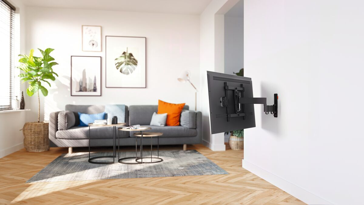 Wohnzimmer mit an der Wand montiertem Fernseher, Sofa und zwei Couchtischen. Holzboden.