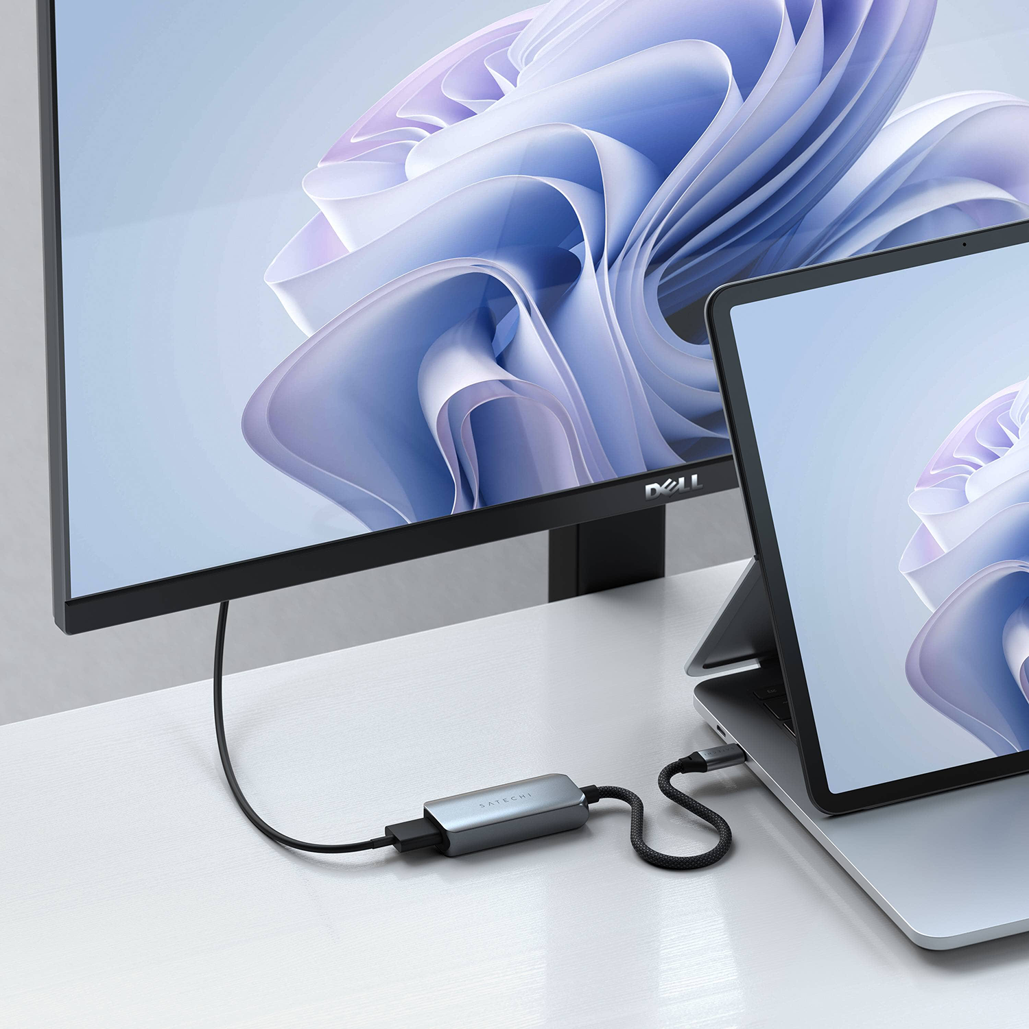 Laptop és monitor ezüst adapterrel csatlakoztatva fehér asztalon.