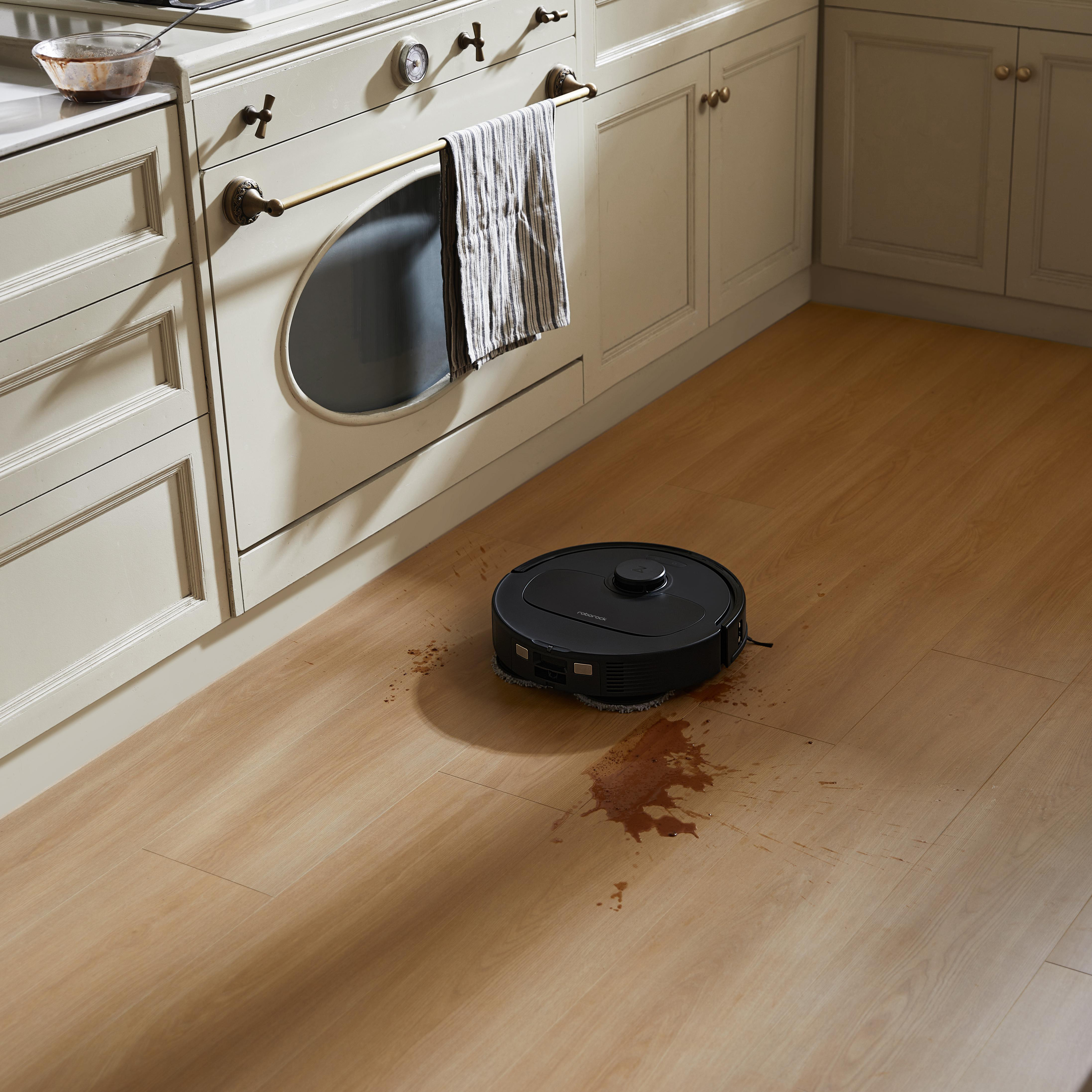 Ein schwarzer Roboter-Staubsauger auf einem Holzboden mit Fleck.