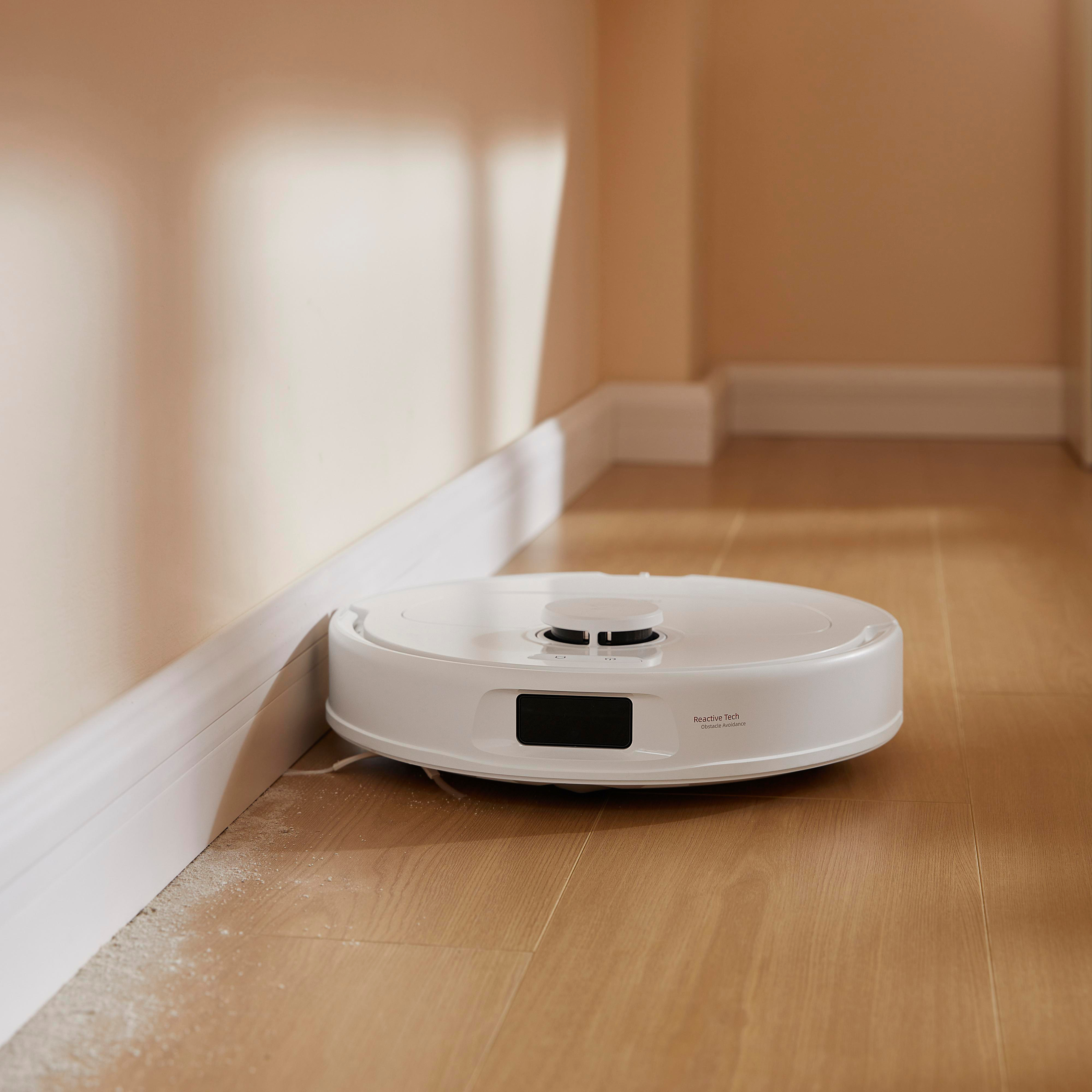 Weißer Roboter-Staubsauger in der Nähe einer Wand auf einem Holzboden.