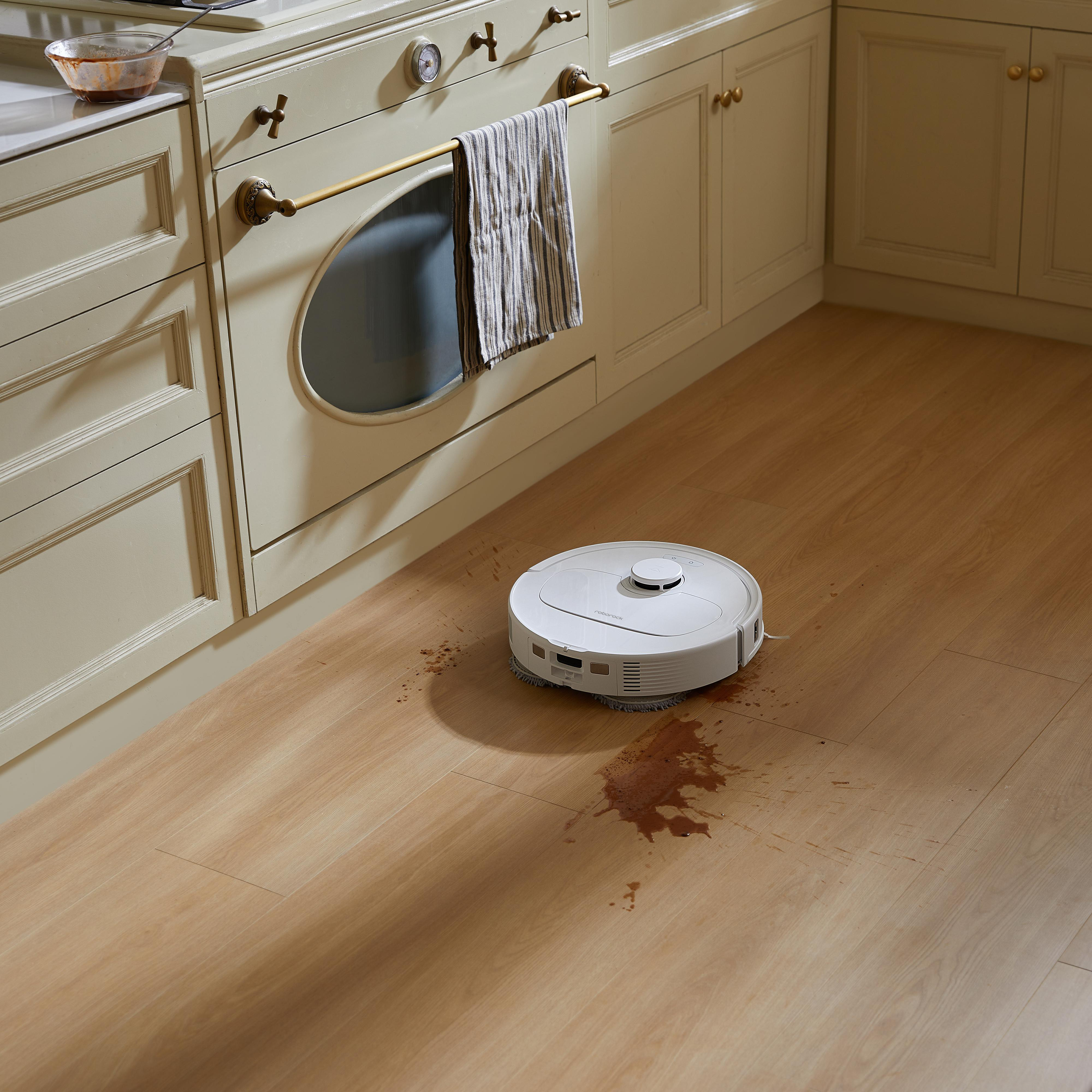 Ein weißer Roboter-Staubsauger auf Holzboden mit verschüttetem Essen.