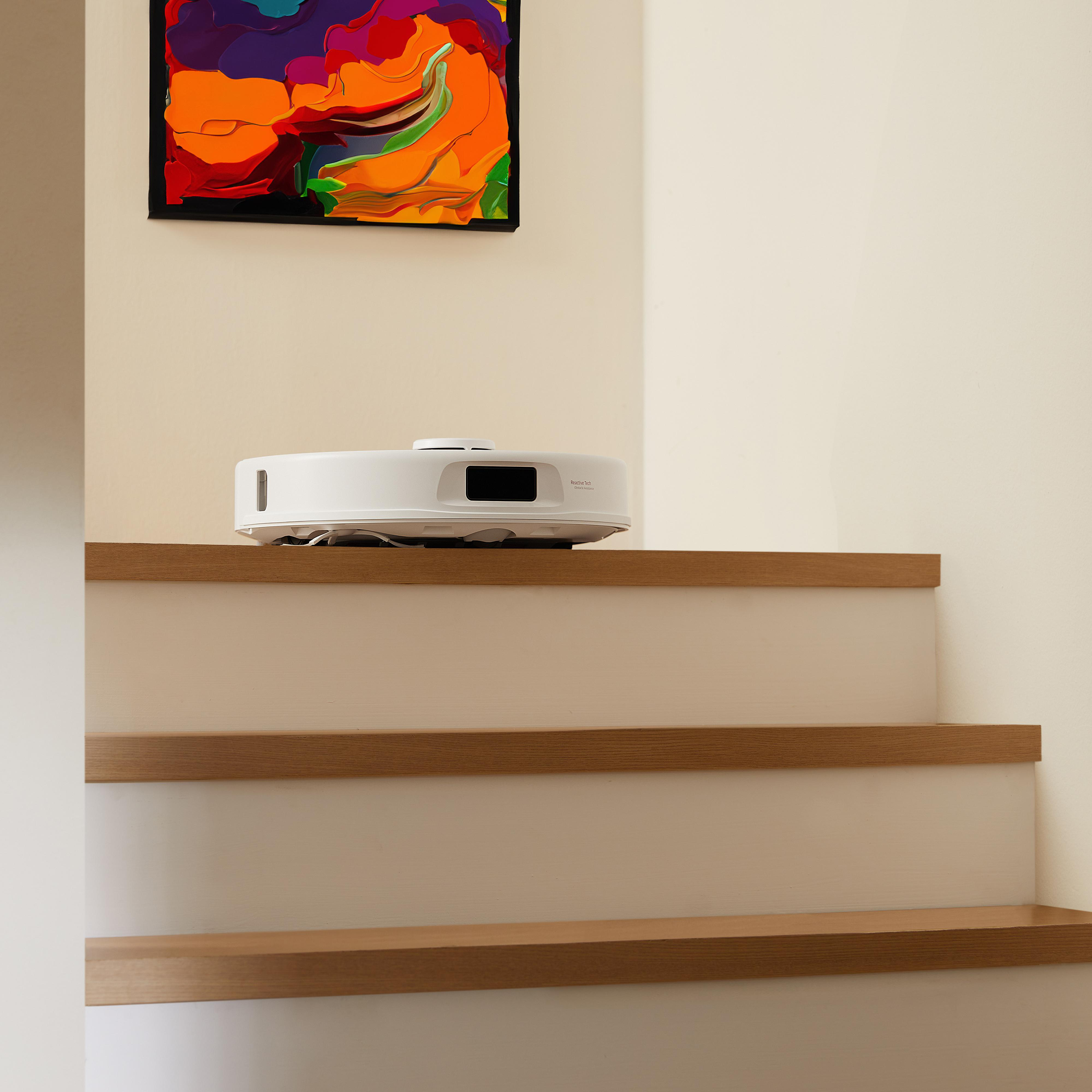 Ein Roboter-Staubsauger auf Holztreppen, ein Gemälde an der Wand. Die Treppe ist aus Holz und weiß.
