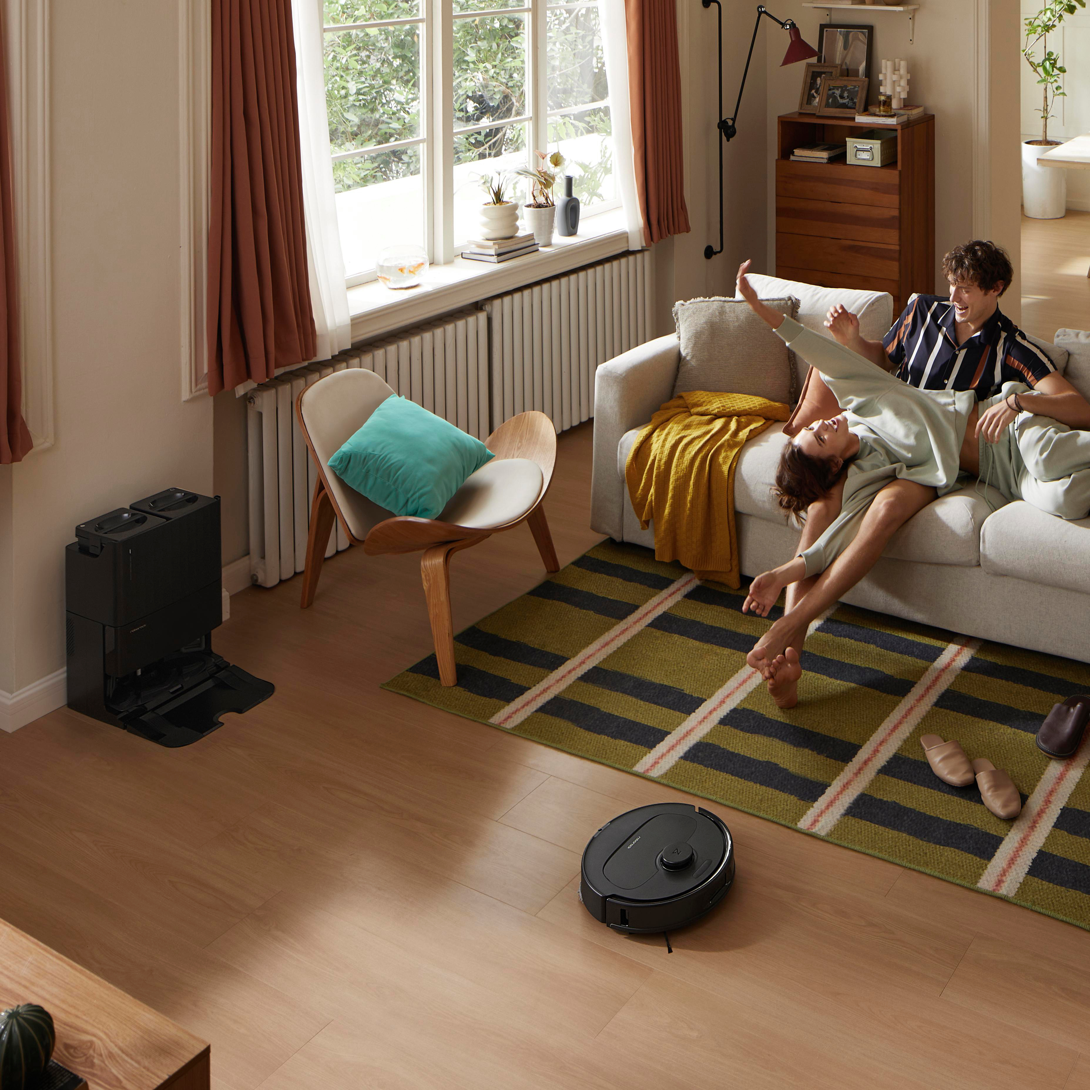 Wohnzimmerszene. Ein Roboter-Staubsauger steht auf dem Boden, Menschen auf einem Sofa.