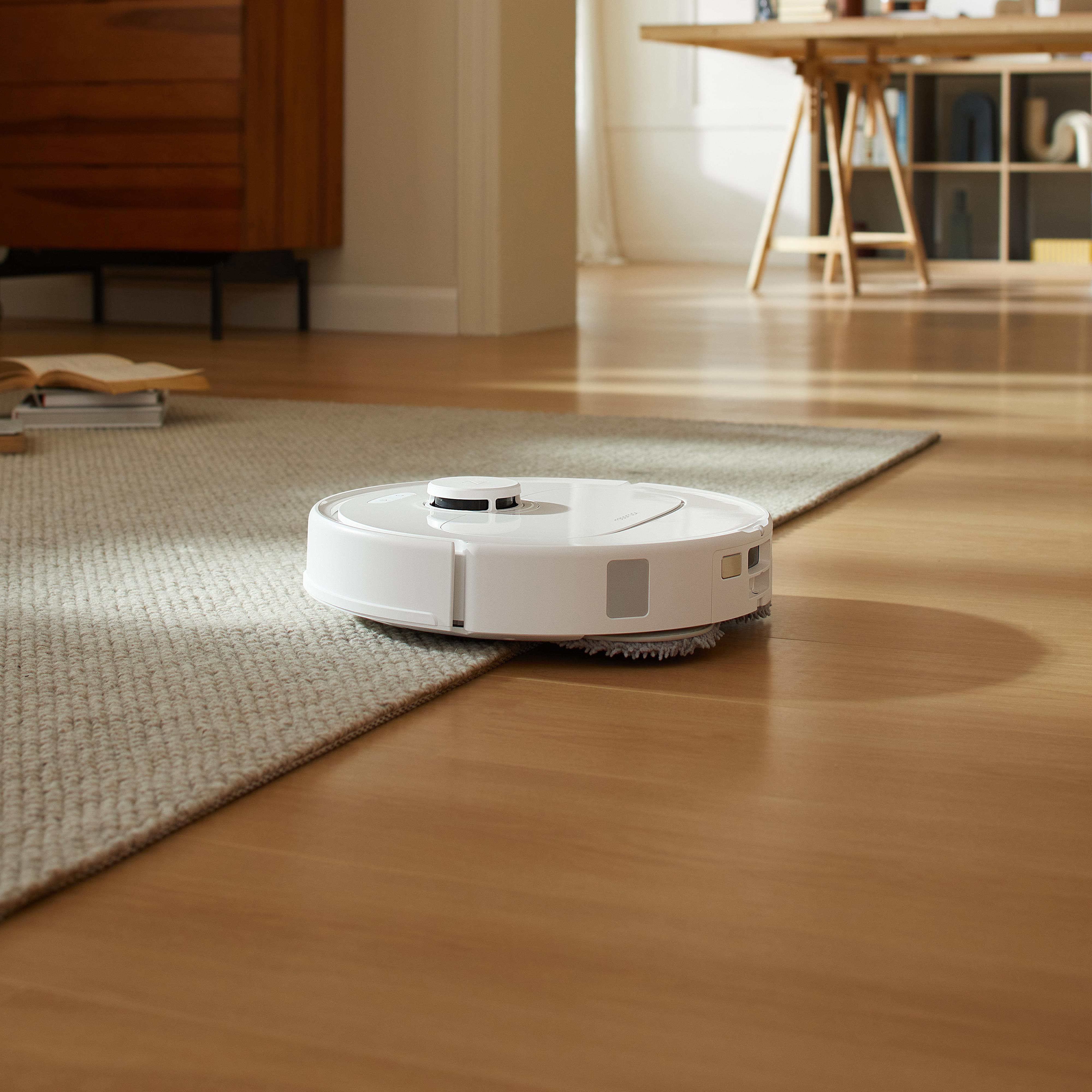 Ein Roboter-Staubsauger auf einem Holzboden, der auf einen Teppich übergeht. Raumumgebung.
