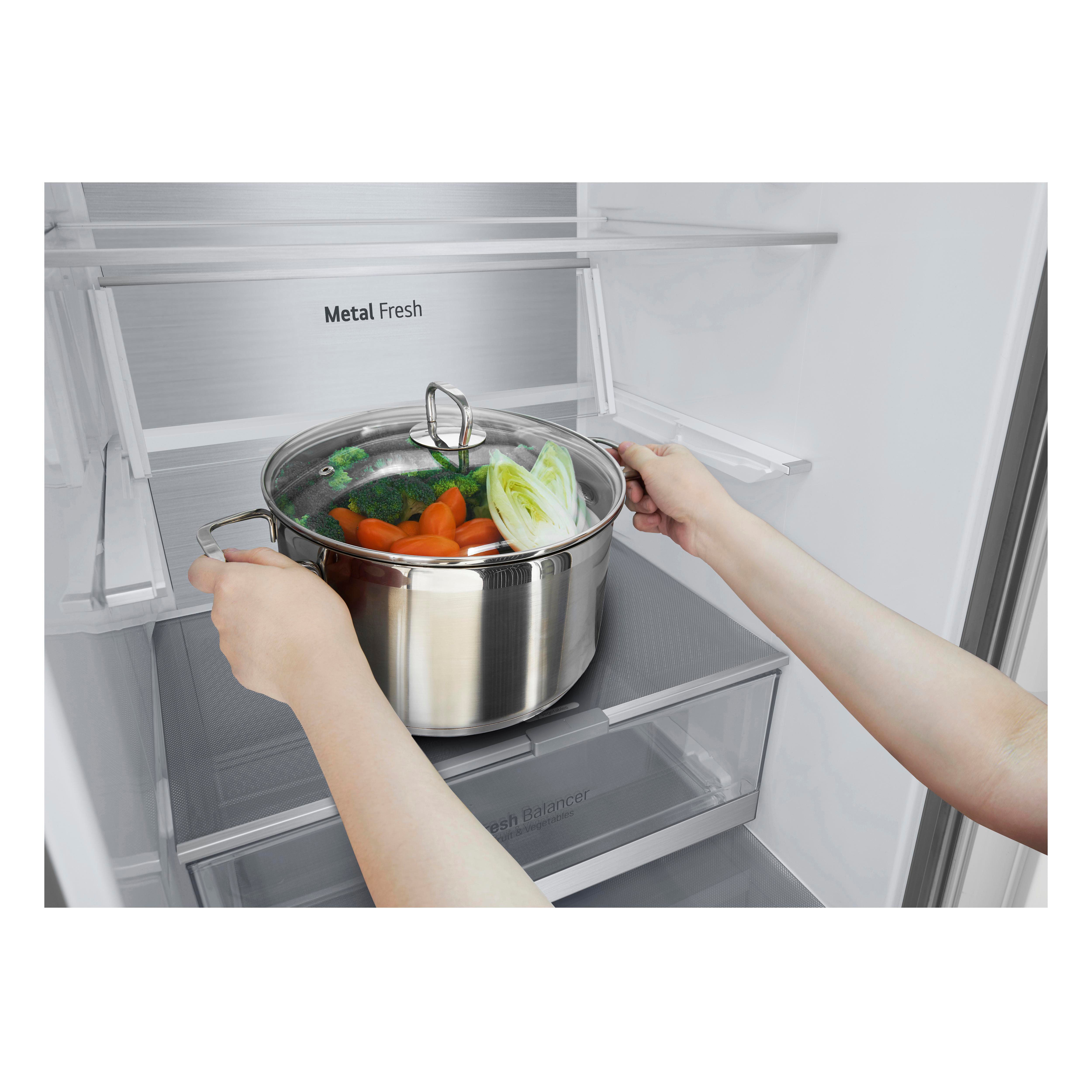 Hände, die einen Metalltopf mit Gemüse in einen Kühlschrank stellen.