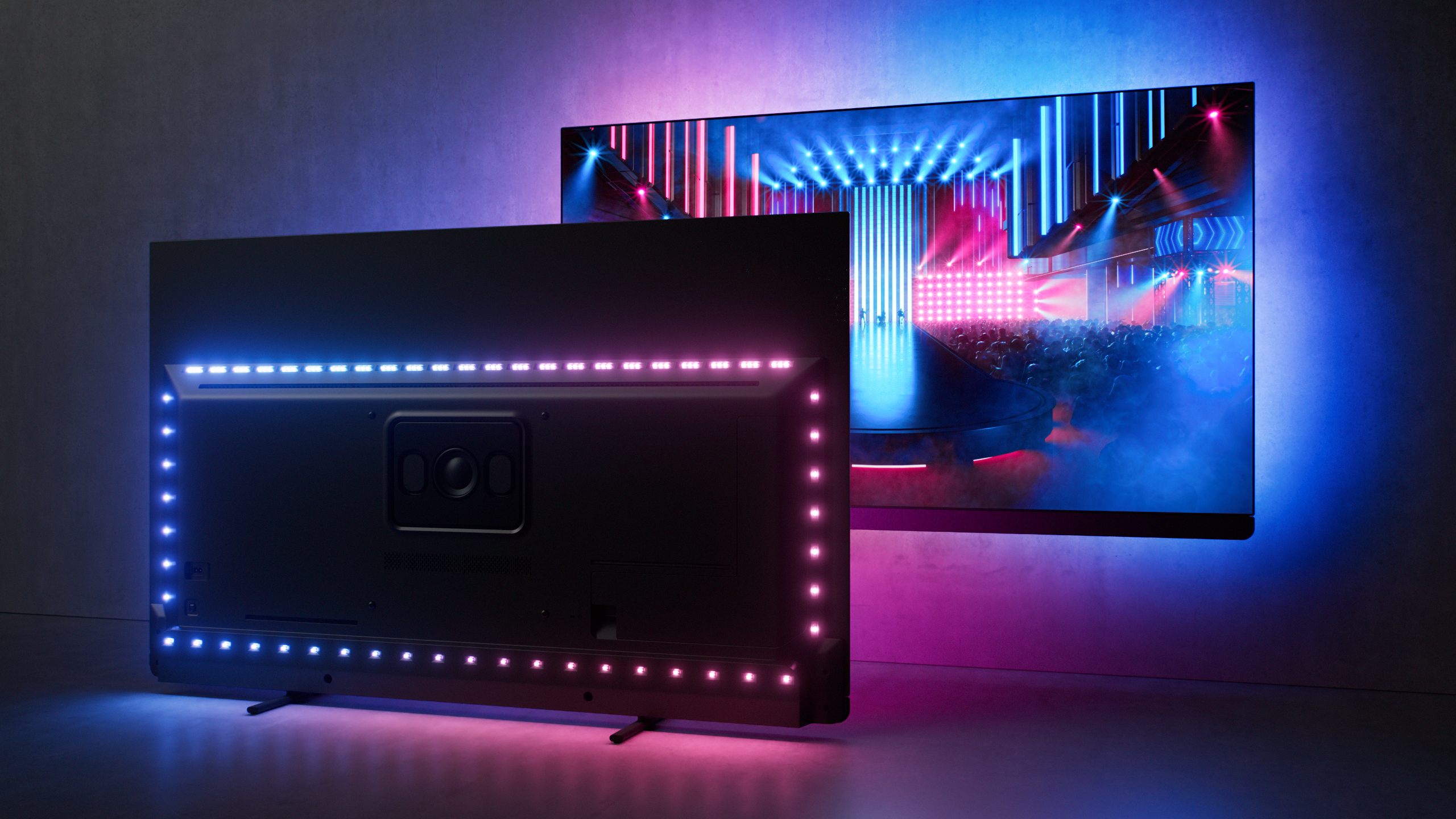 Due TV che mostrano contenuti, una con luci a LED sul retro, contro un muro grigio.