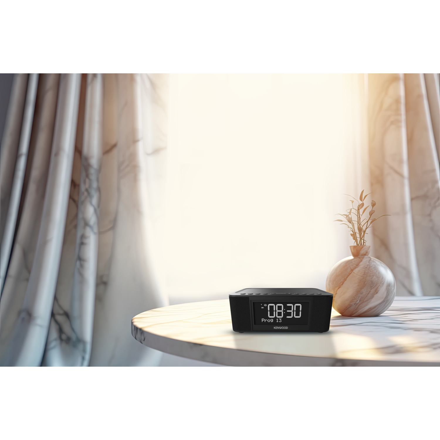 Black clock on a table, showing 08:30. A vase with plants and curtains are in the background.