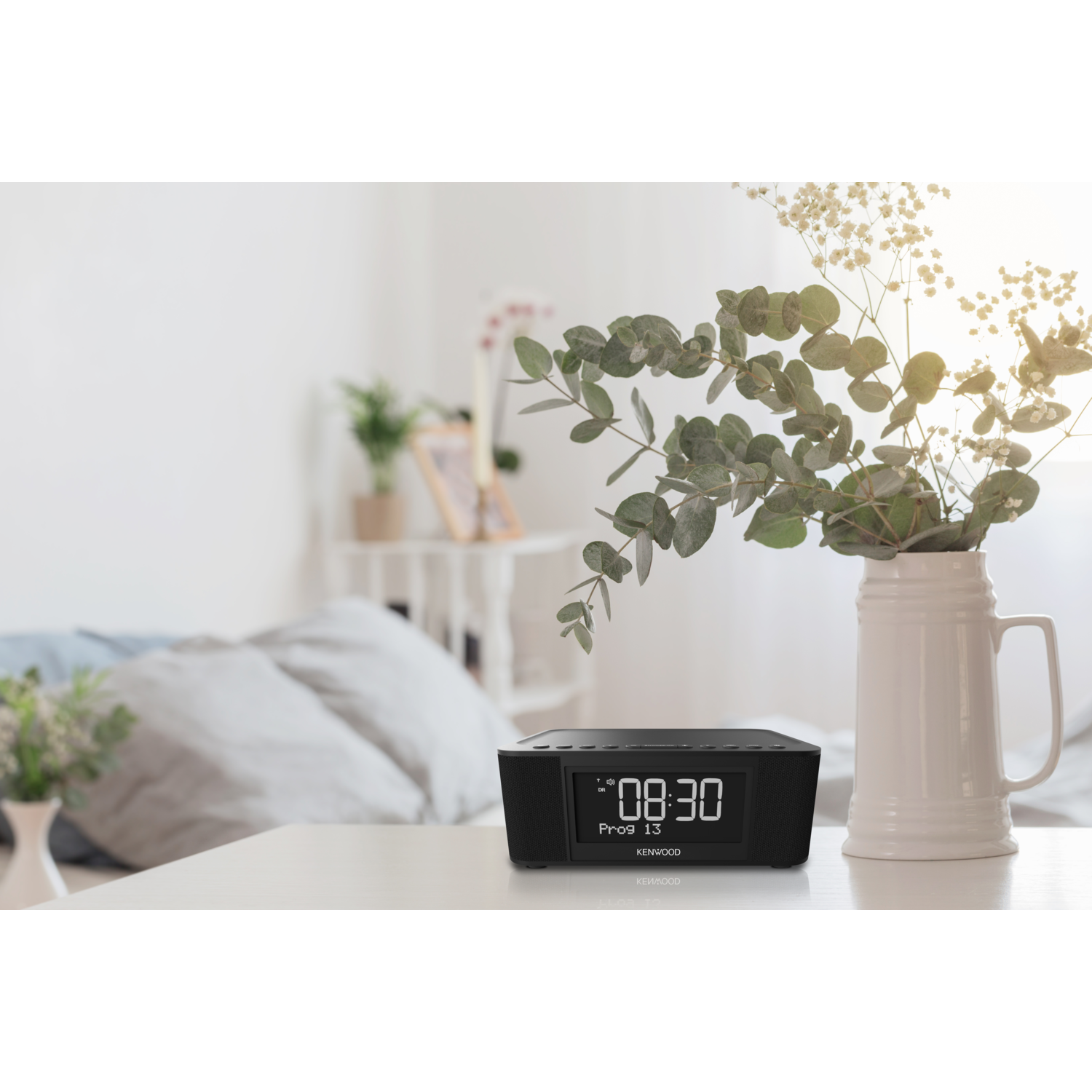 Black digital alarm clock with a vase of flowers on a white table.