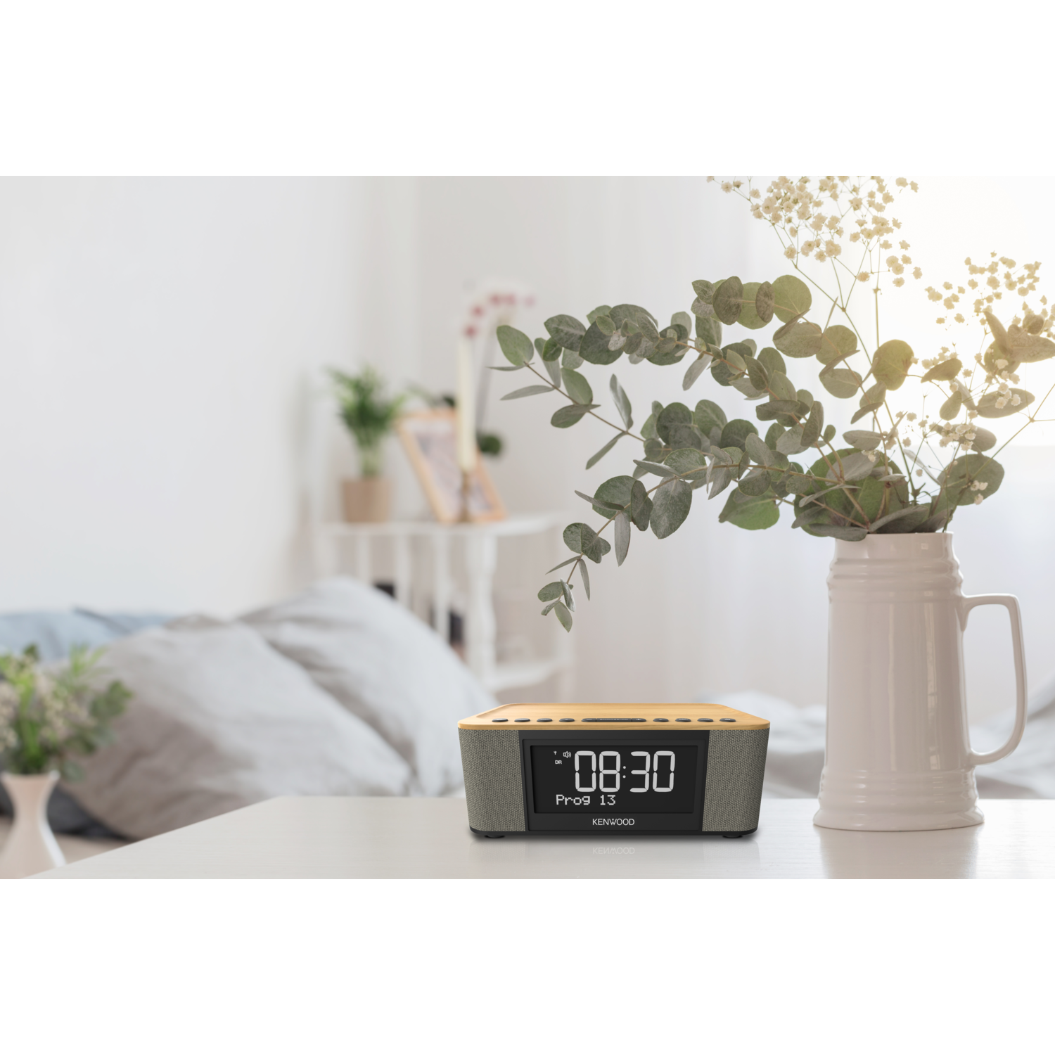 Alarm clock on a table. A vase with flowers is in the background. The clock shows 08:30.