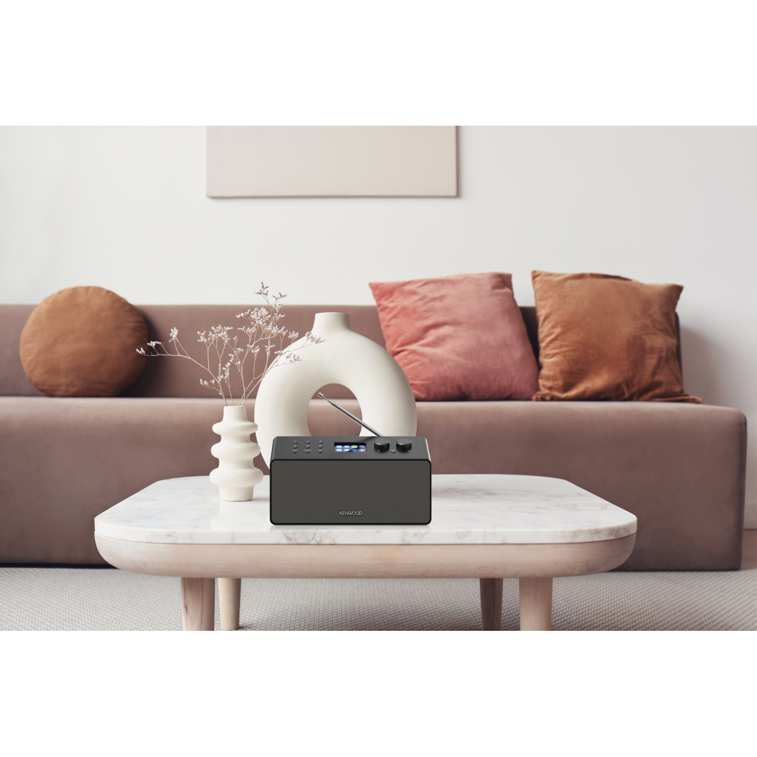 A radio on a table. There is a vase and pillows on the table.