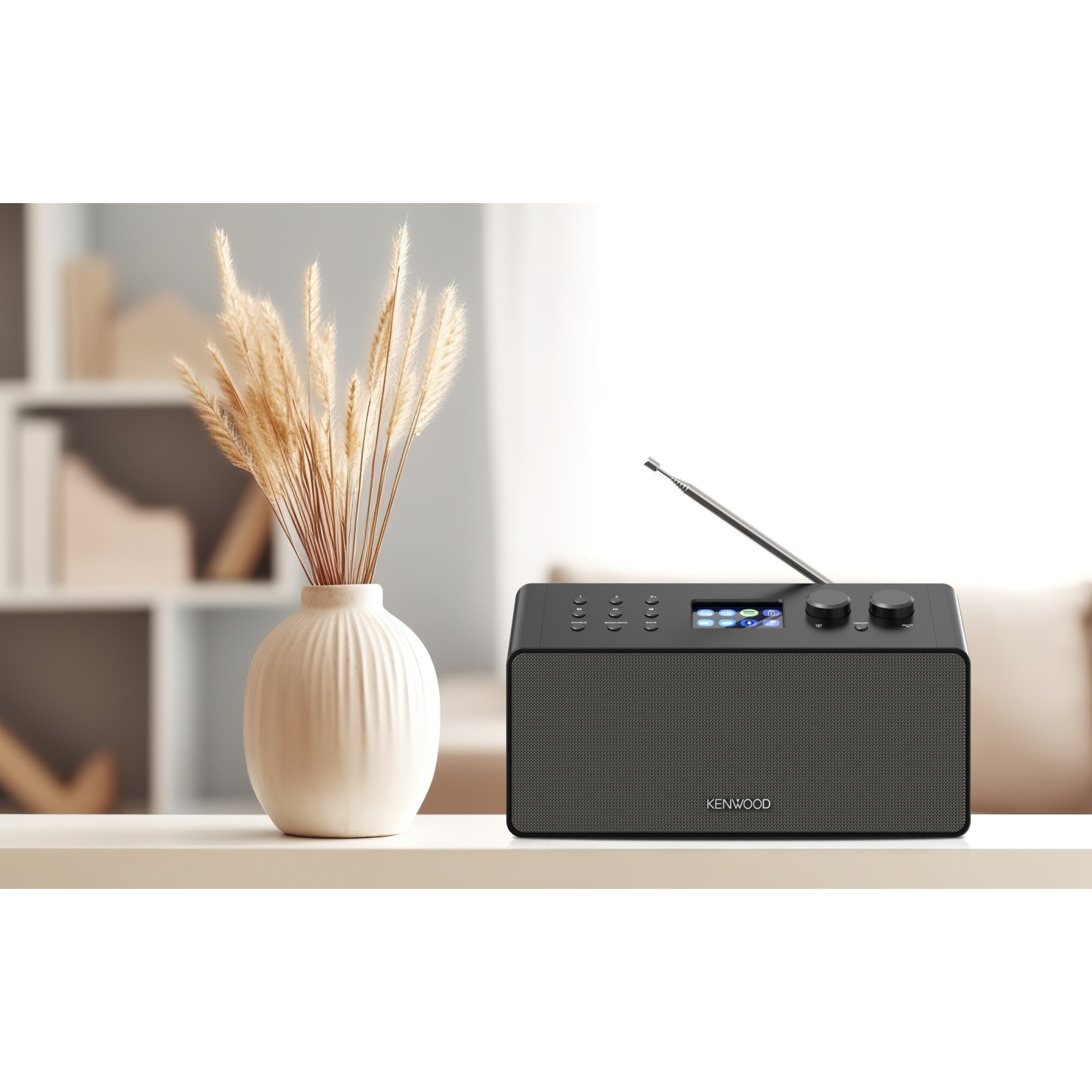 Kenwood radio on a table with a vase and a plant. The radio has a digital display and antenna.