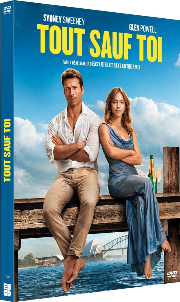 Filmaffiche: 'Anyone But You'. Een man en een vrouw staan op een pier. Blauwe lucht en water op de achtergrond.