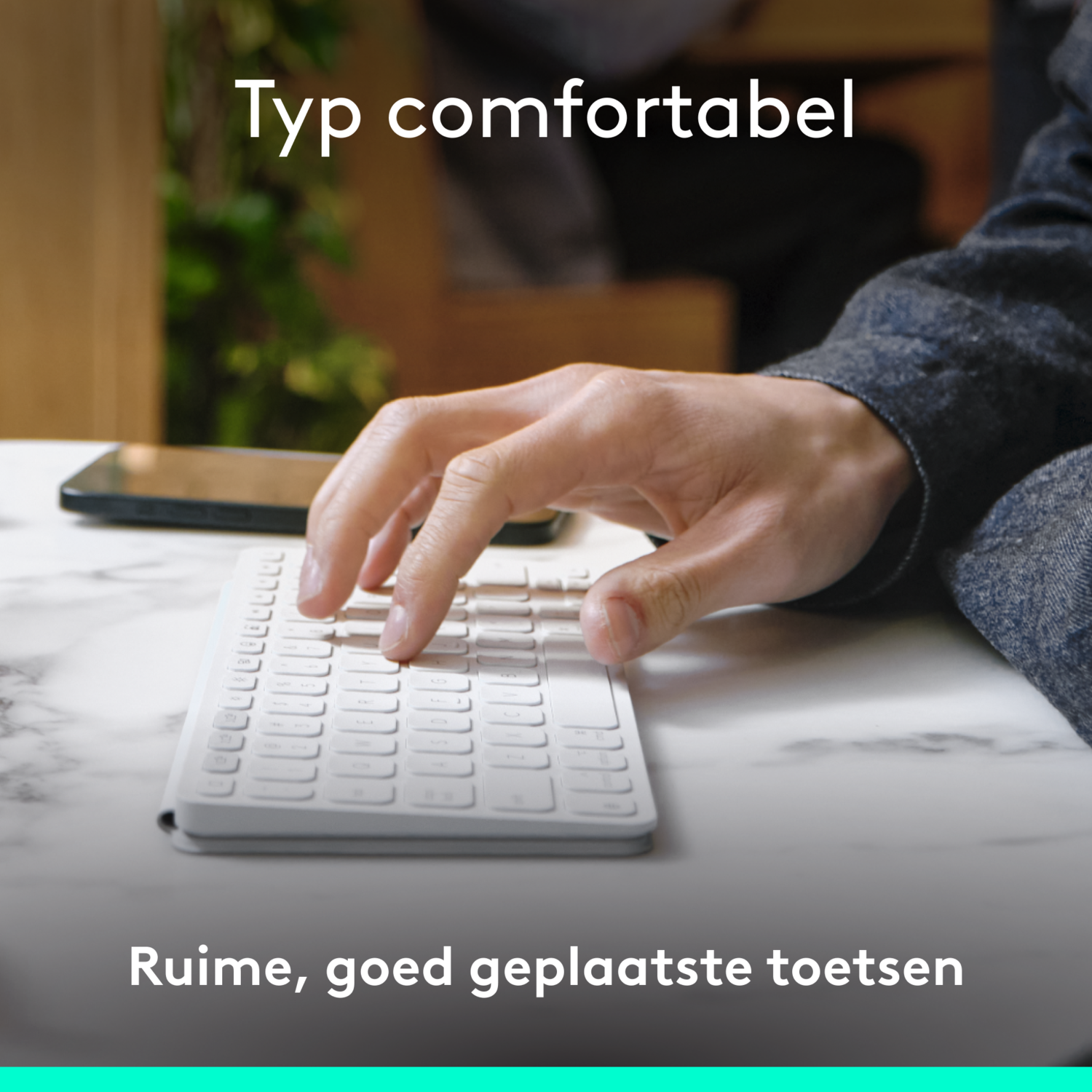 A person's hand using a white keyboard on a marble surface, text reads 'Typ comfortabel'.