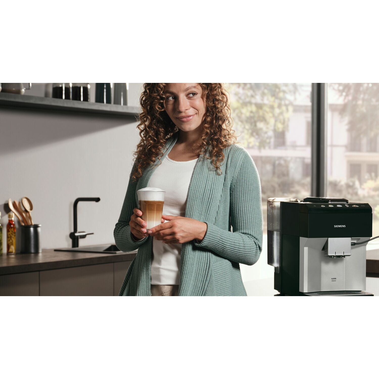 Femme tenant un verre de latte macchiato près d'une machine à café. Fond de cuisine.