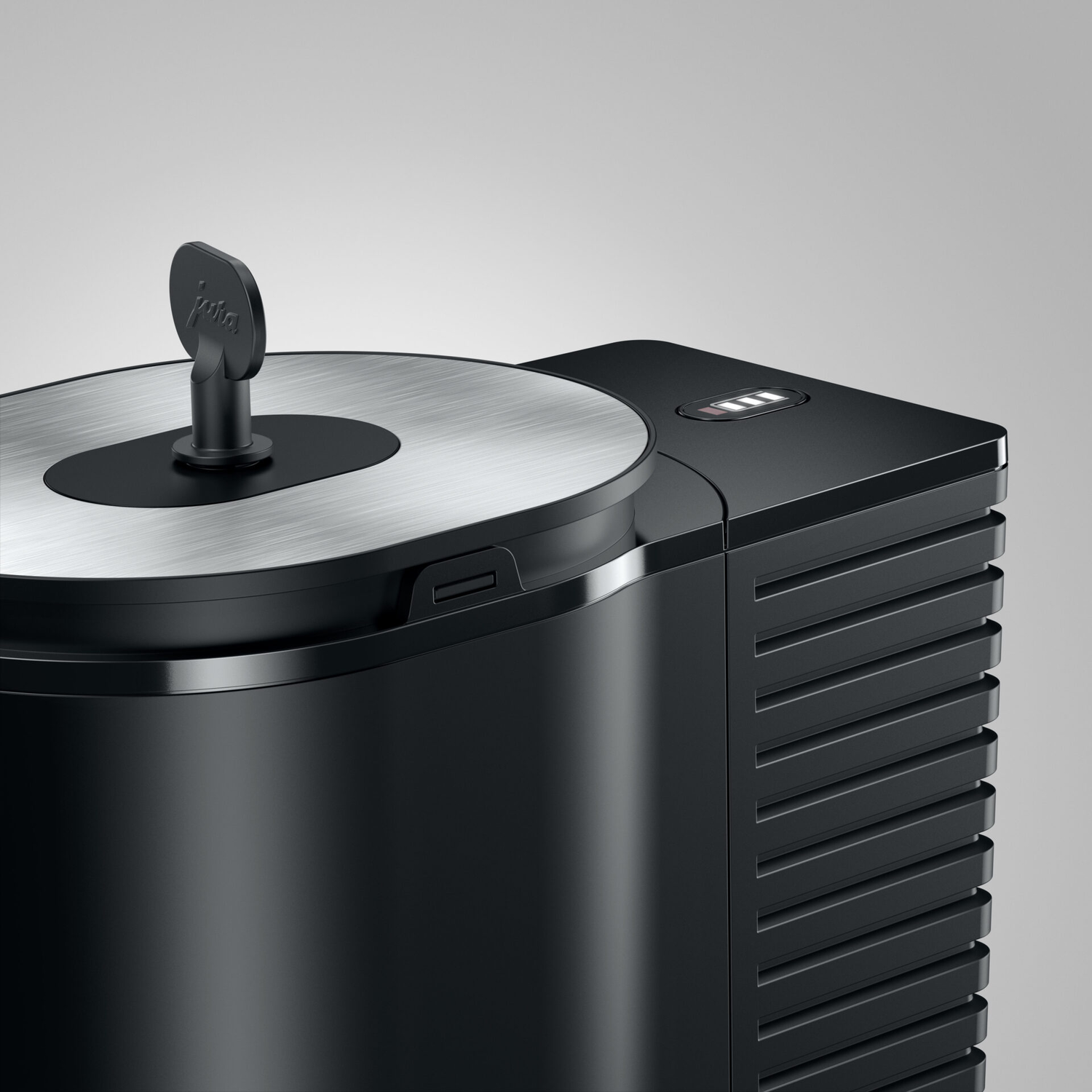 Close-up of a black coffee machine with a silver lid and the Jura logo on top.