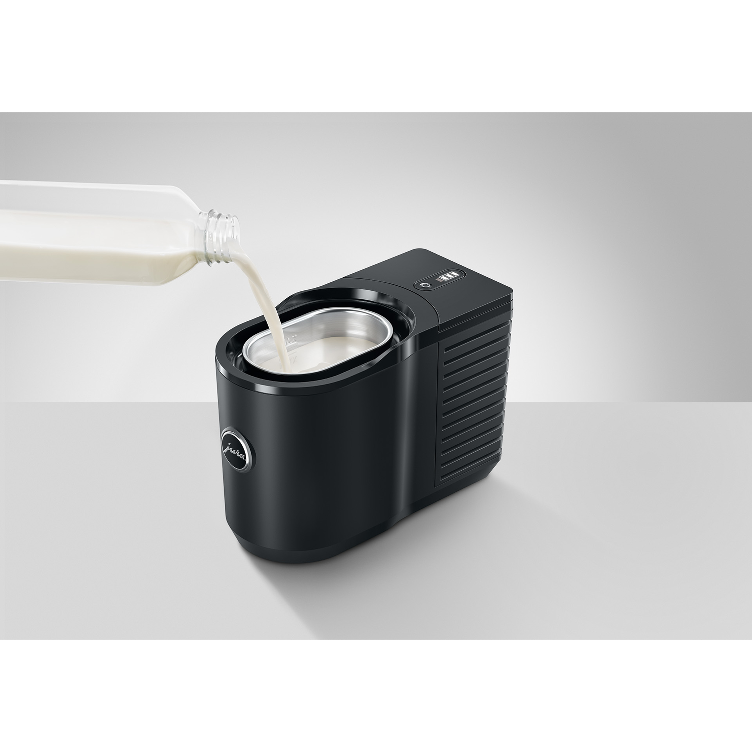 A black device with milk being poured into it. The device is on a white surface.
