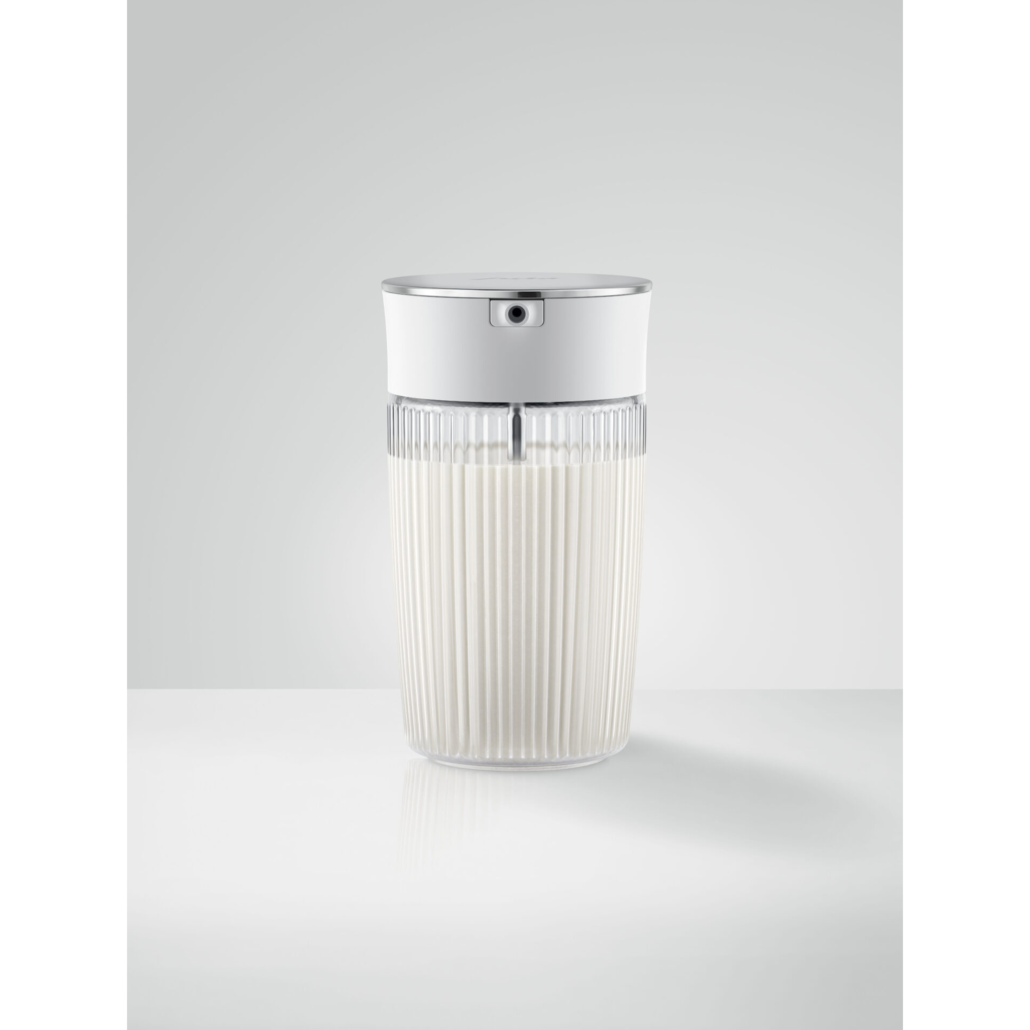 Een witte melkopschuimer met een helder, geribbeld glas met witte melk opgeschuimd.