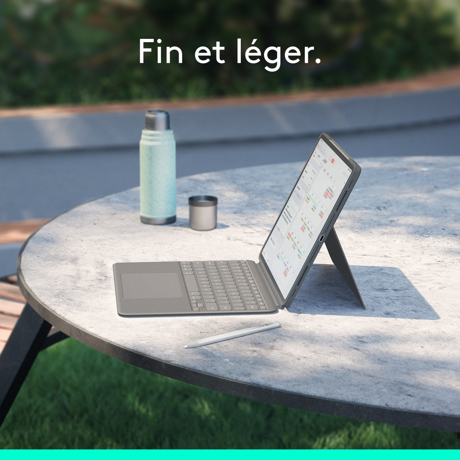 Une tablette avec clavier sur une table ronde, avec un thermos et une tasse à l'extérieur.