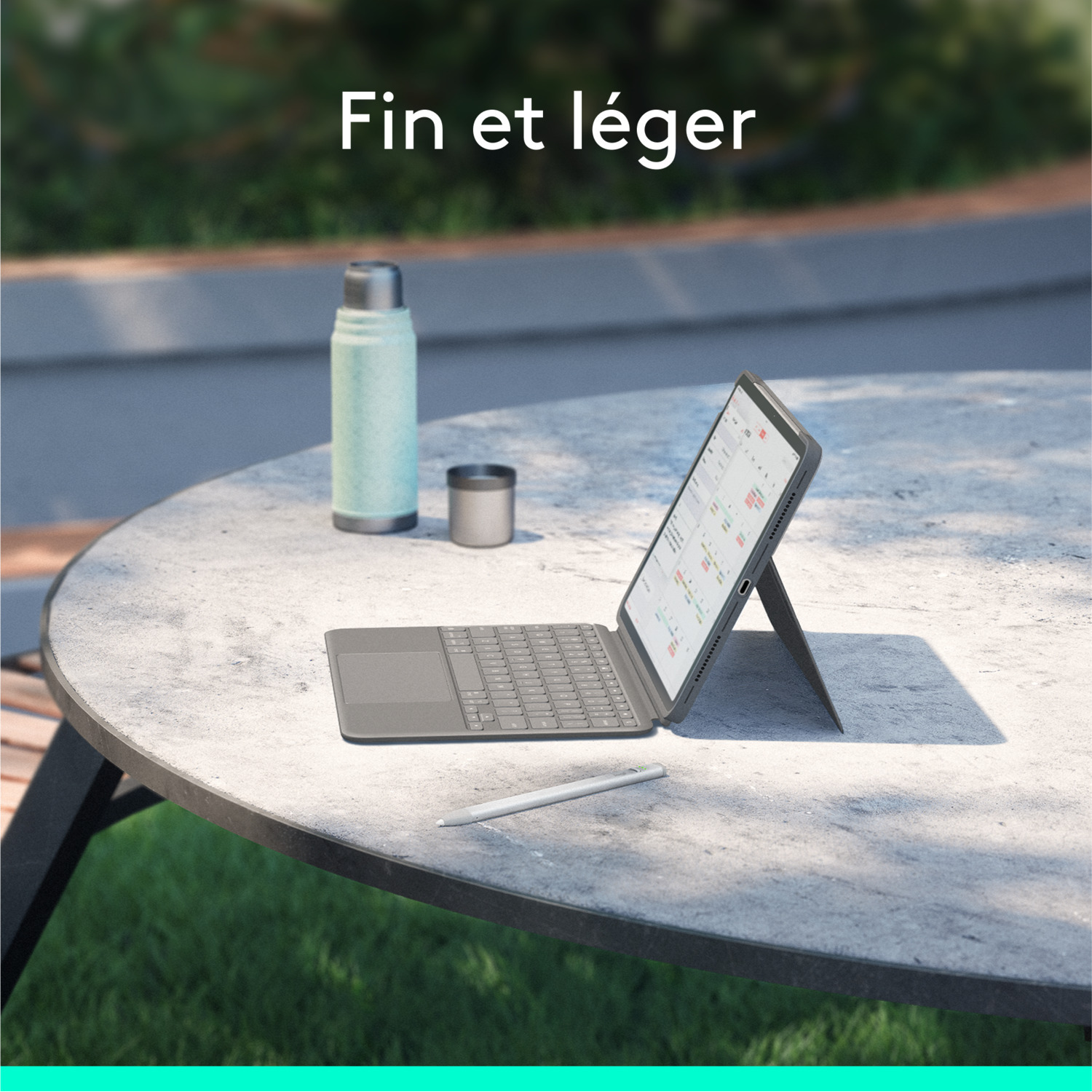 Tablette avec clavier et stylo sur une table à l'extérieur.