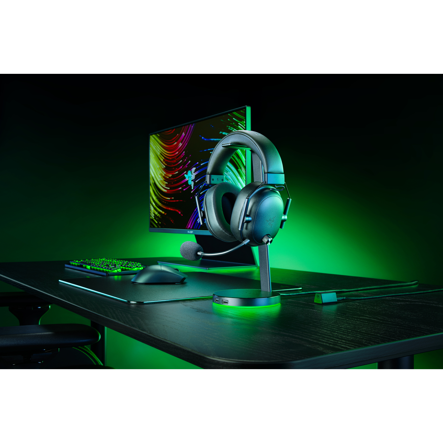 Gaming setup with headphones on a stand, keyboard, mouse, and a monitor displaying a green and black image.