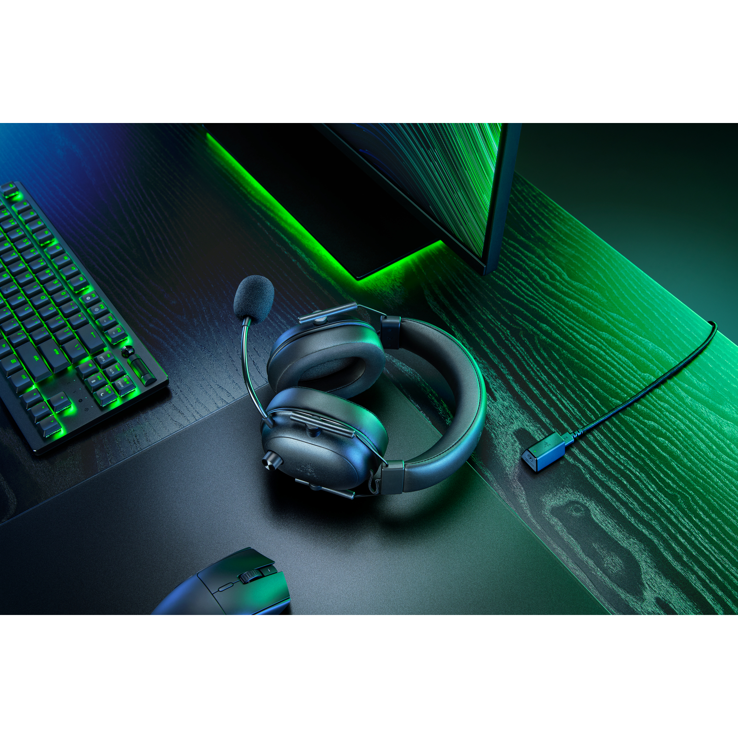 Black gaming headset and mouse on a dark desk. A keyboard and monitor are also visible.