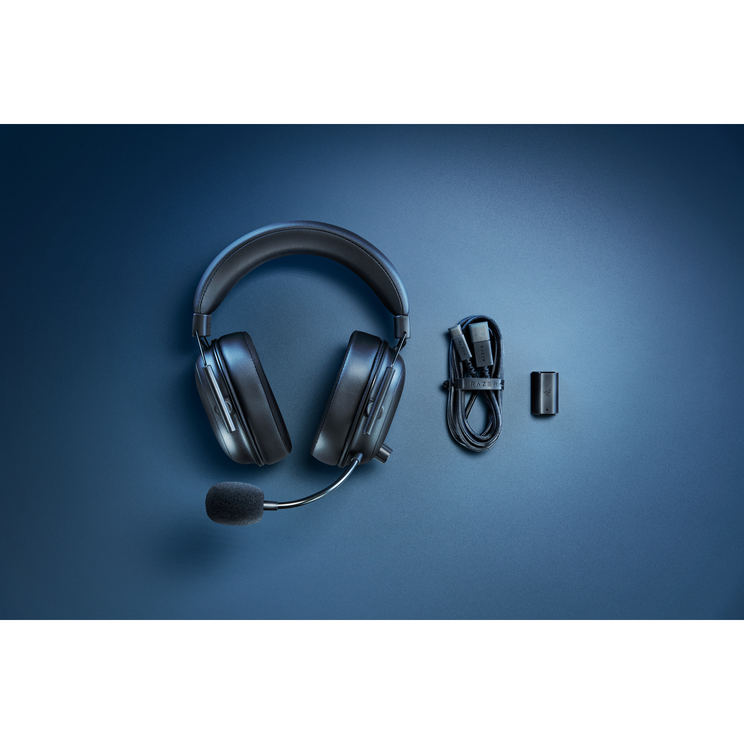 Black wireless gaming headphones with a microphone and charging cable, on a blue surface.