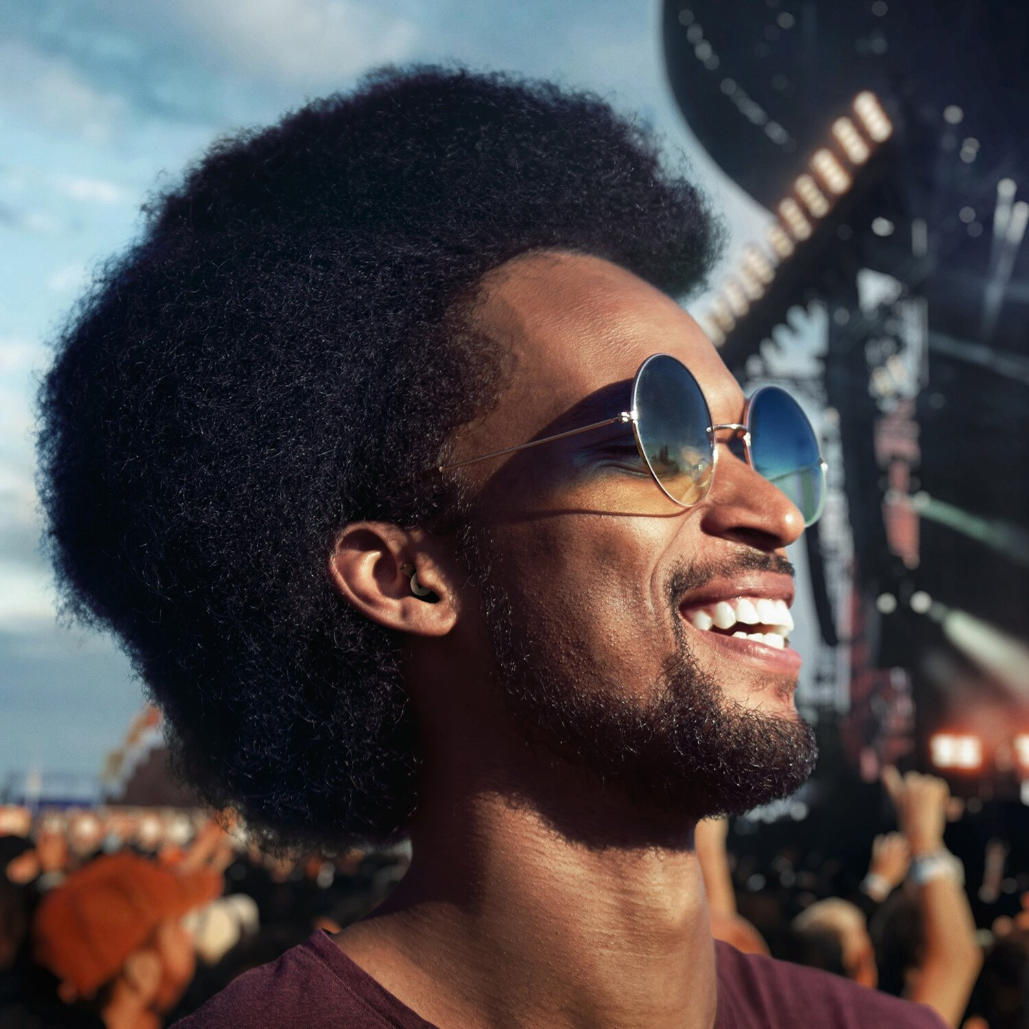 Homme souriant portant des lunettes de soleil et un écouteur lors d'un concert.