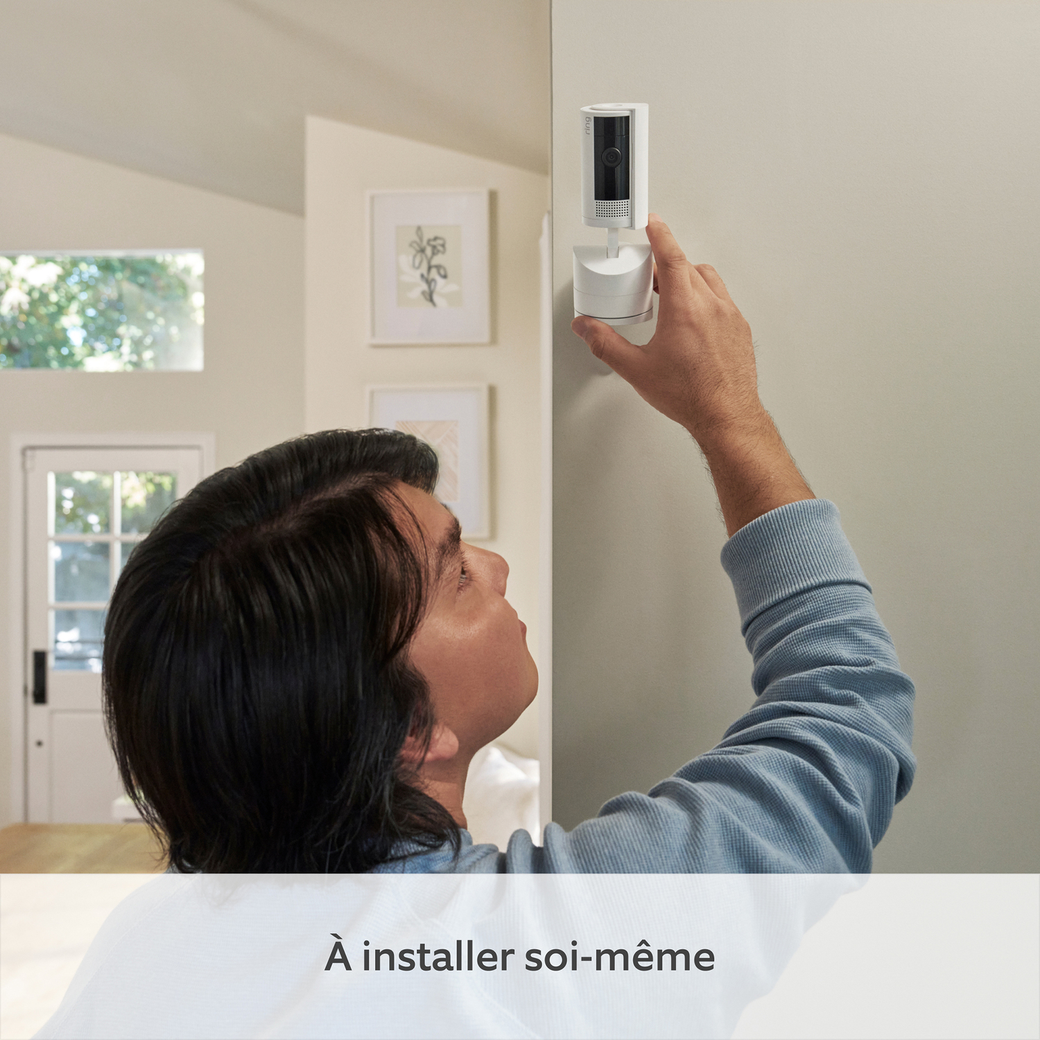 Homme installant une caméra de sécurité sur un mur. Il regarde la caméra.
