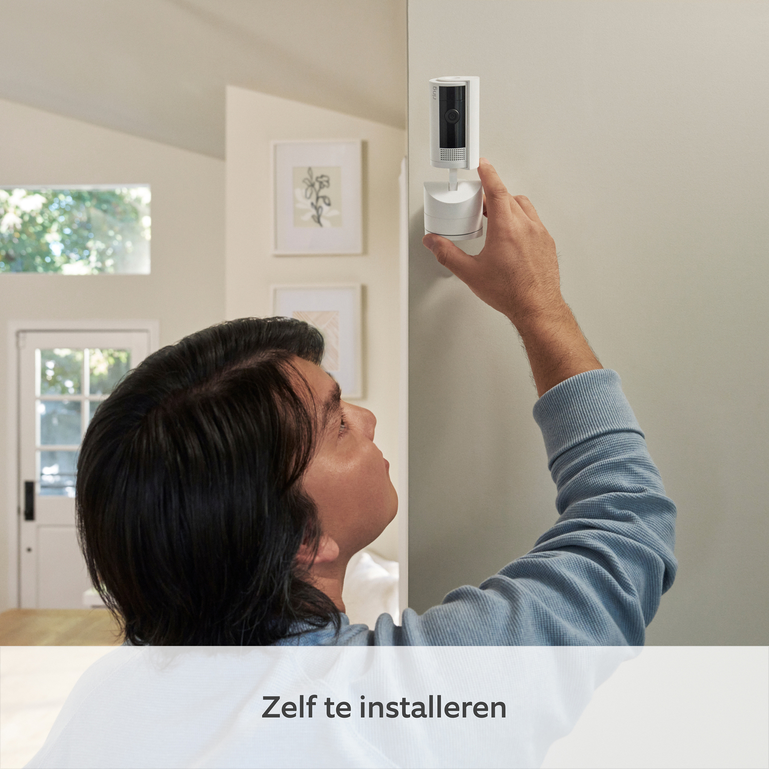 A person installing a white security camera on a wall, with text in Dutch below.