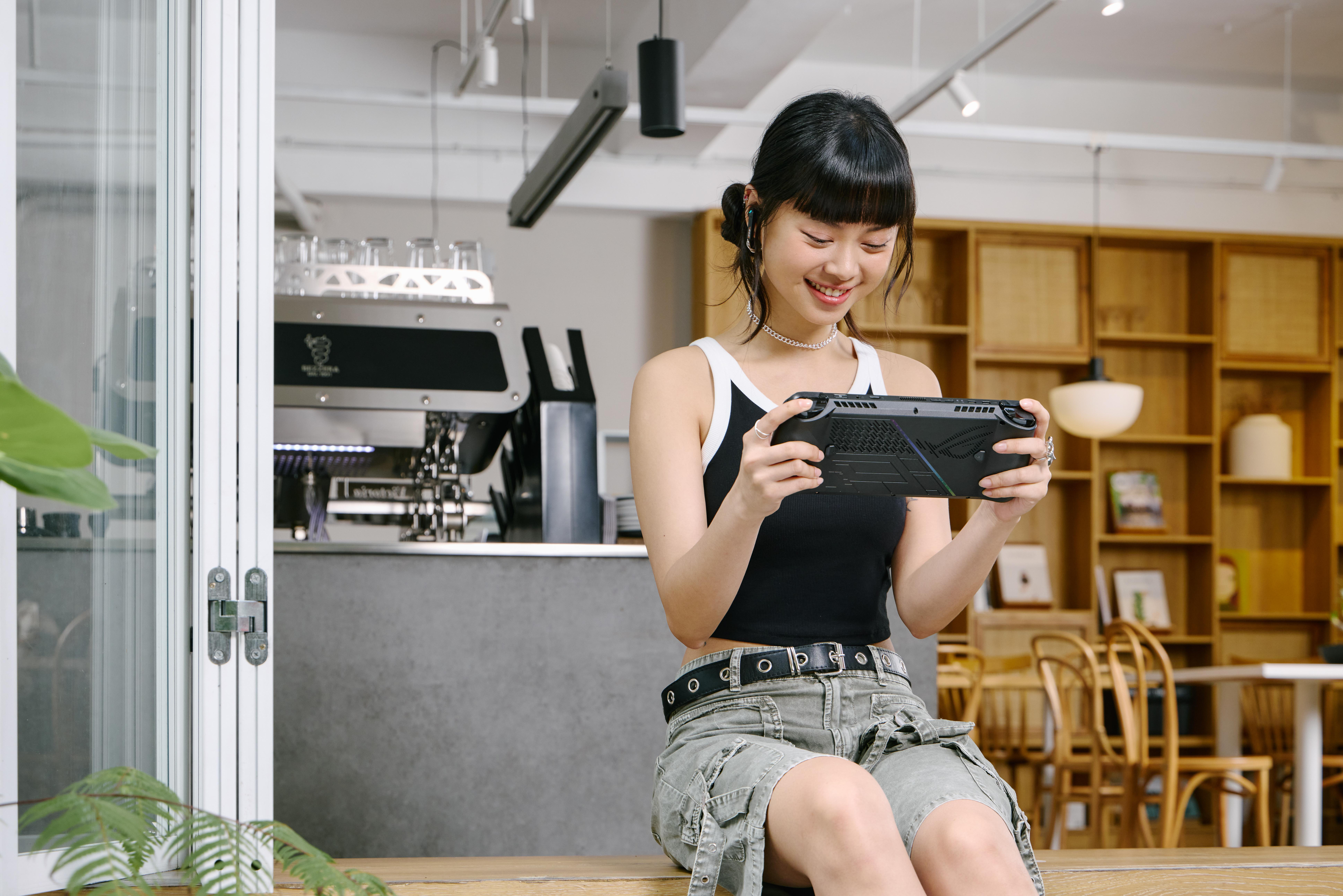 Junge Frau sitzt, lächelt und hält ein Handheld-Spielgerät. Kaffeehaus-Einstellung.