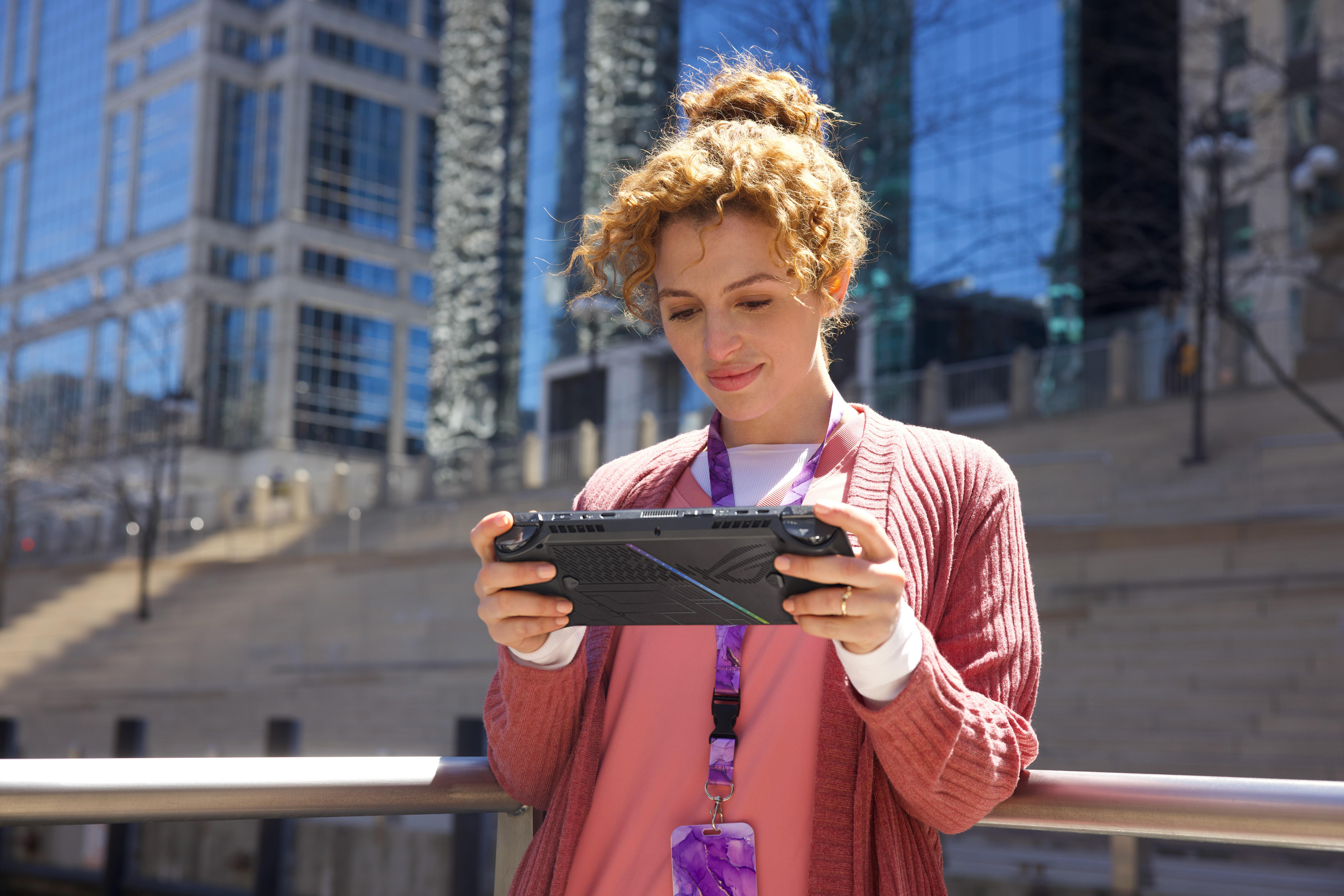 Frau mit lockigem Haar, die im Freien ein Handheld-Spielgerät benutzt. Gebäude im Hintergrund.