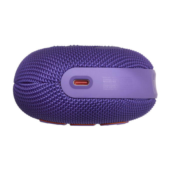 Altavoz JBL morado. El altavoz tiene una cubierta de tela morada y un acento naranja. Puerto USB-C visible.