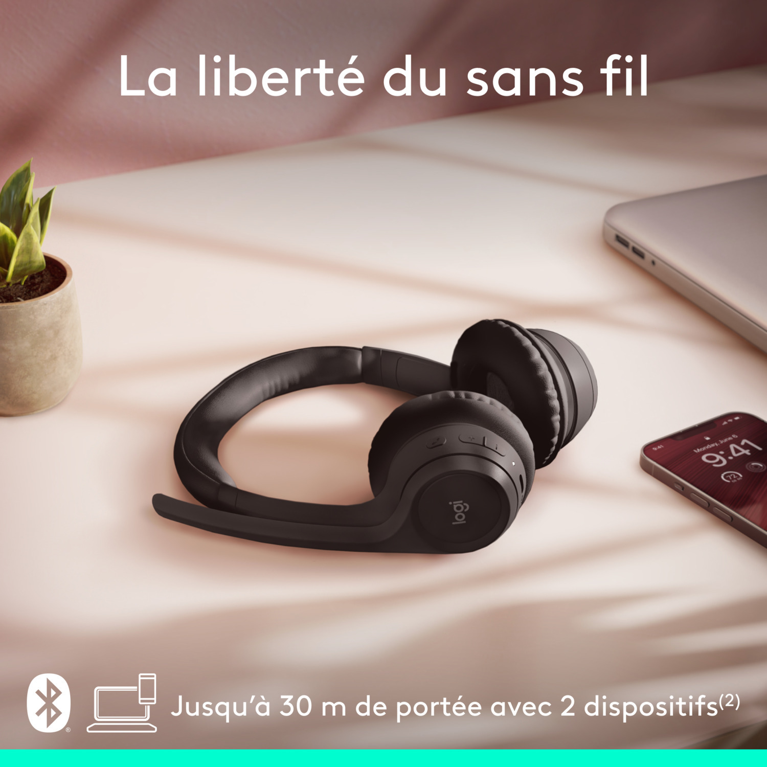 Casque noir sur une surface rose. Un ordinateur portable et un téléphone à proximité. Liberté sans fil.