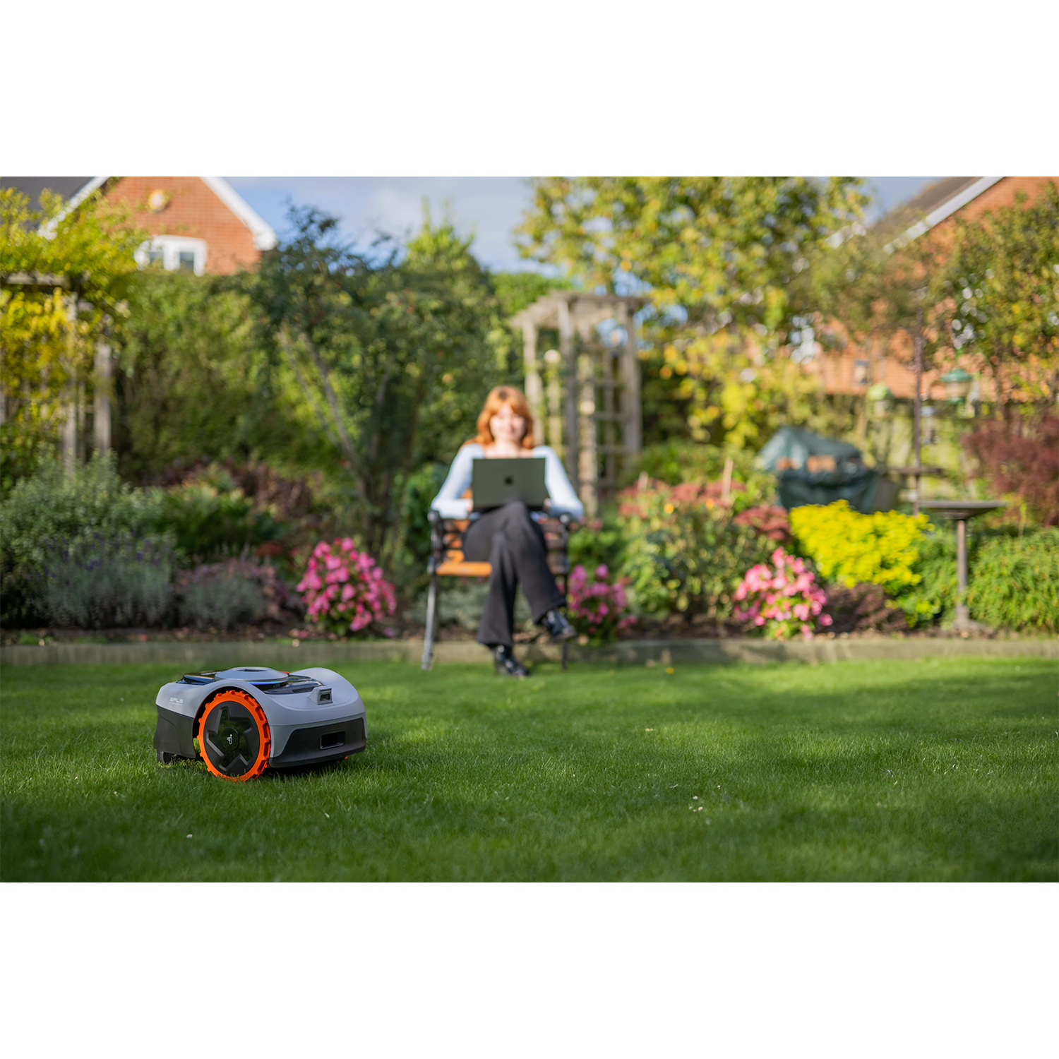 Donna con laptop, robot tosaerba sull'erba, ambiente giardino.