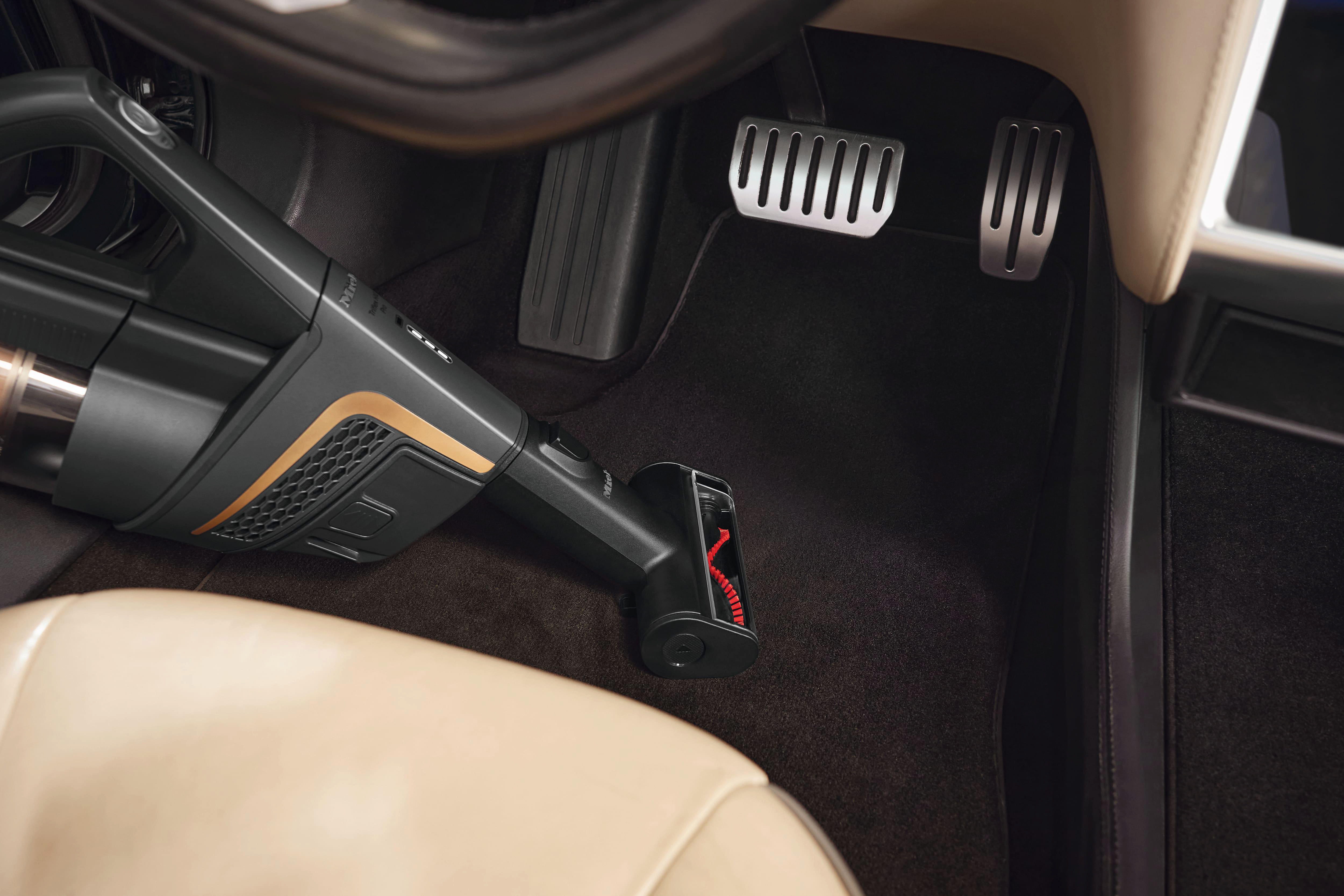 Innenaufnahme eines Autos, schwarzer Teppich mit einem Staubsauger, der den Boden reinigt.