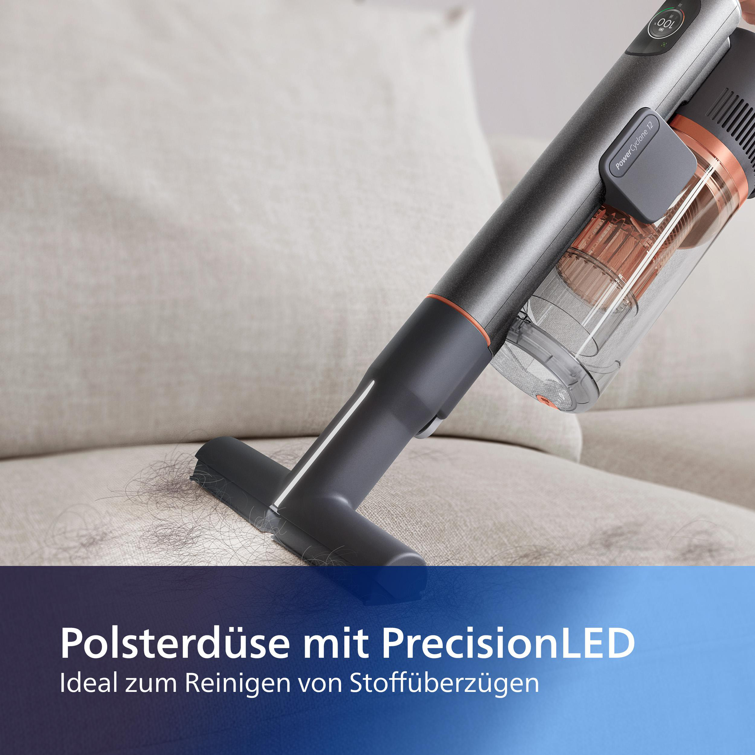 Staubsauger reinigt Sofa, Bürstenkopf auf der Oberfläche. Text sagt 'Polsterdüse mit PrecisionLED'.