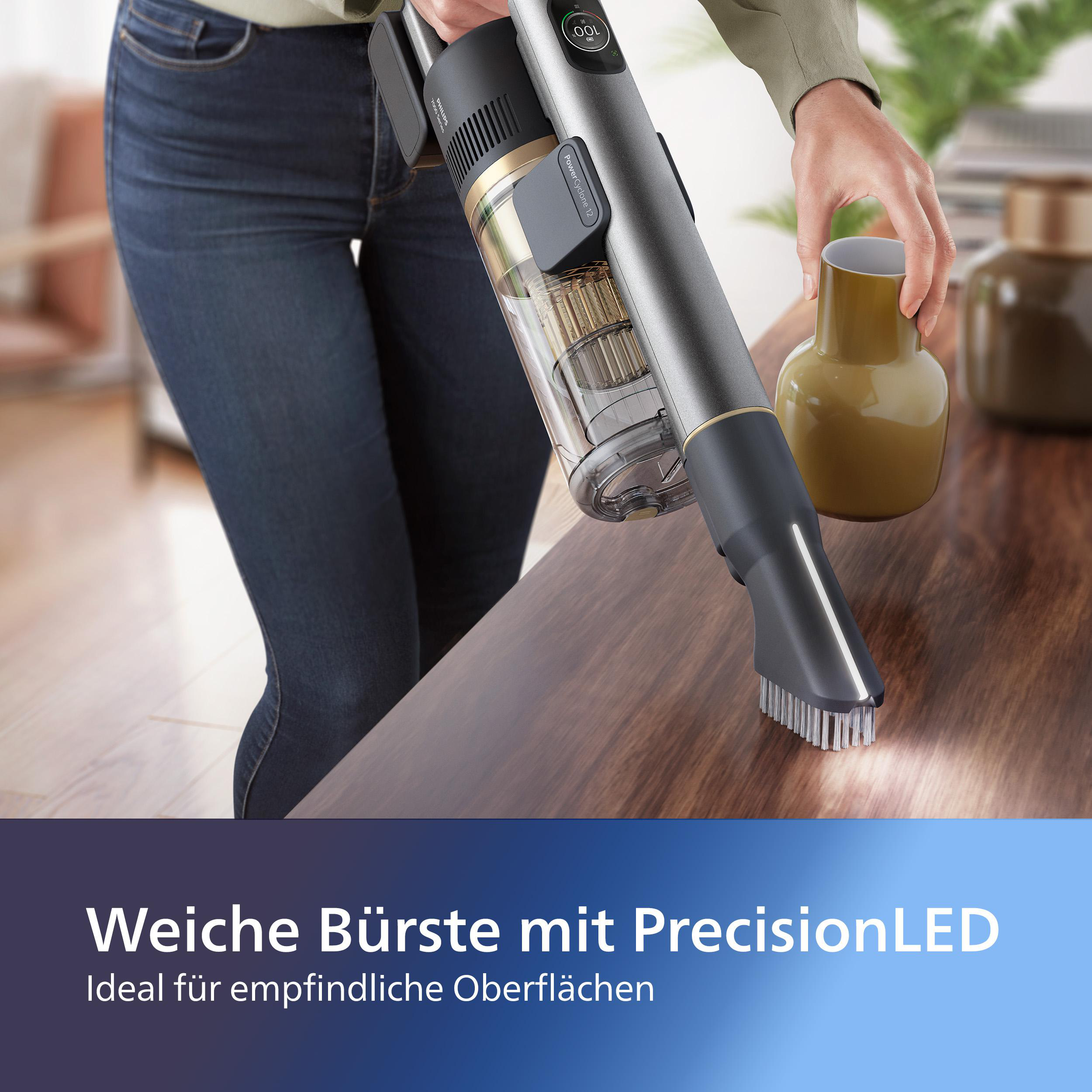 Person benutzt Staubsauger mit Bürstenaufsatz auf einem Holztisch. Text: Weiche Bürste mit Precision-LED.