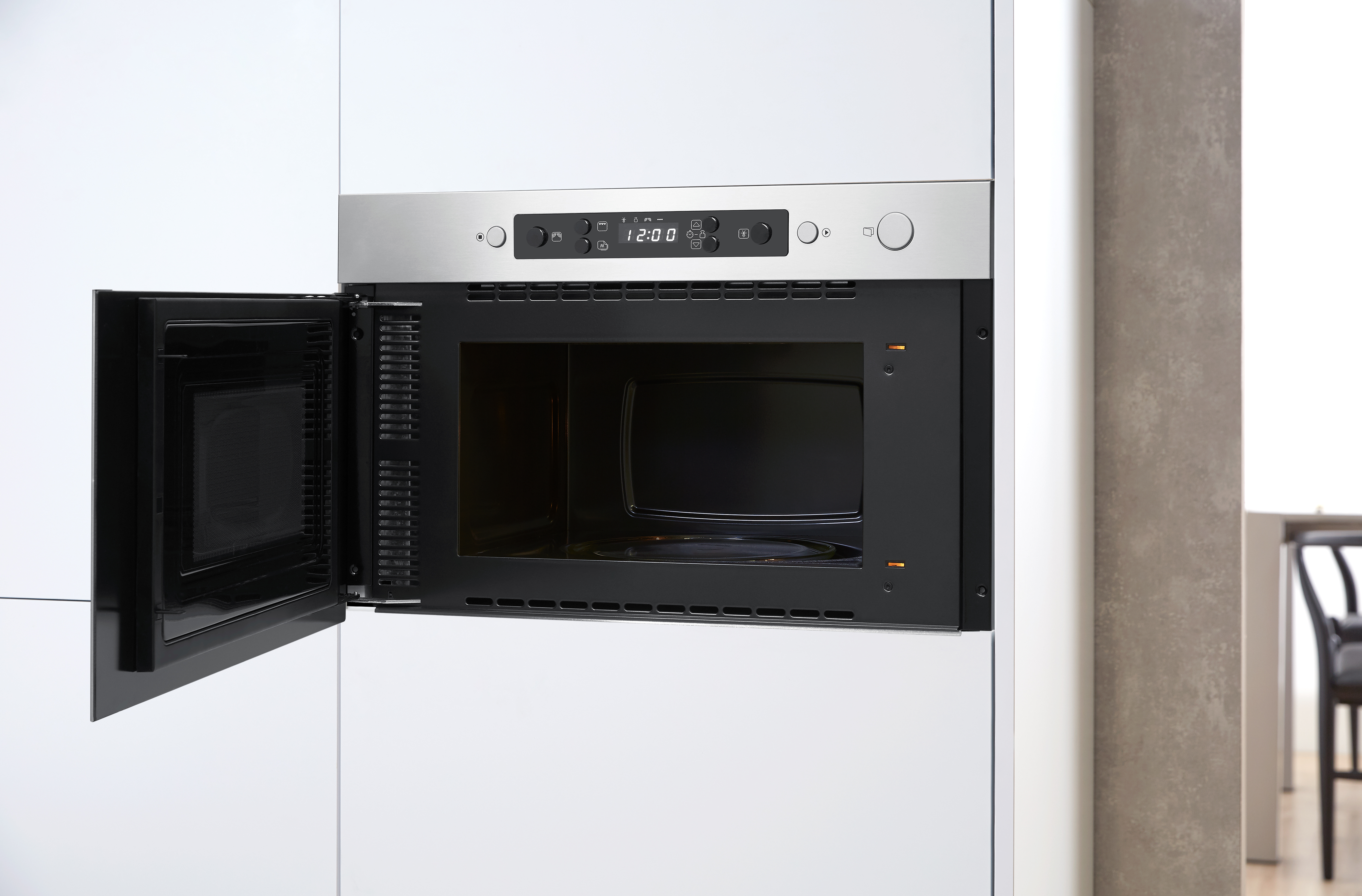 Horno microondas empotrado. Interior negro, puerta abierta. Gabinetes blancos alrededor. Acentos de acero inoxidable.