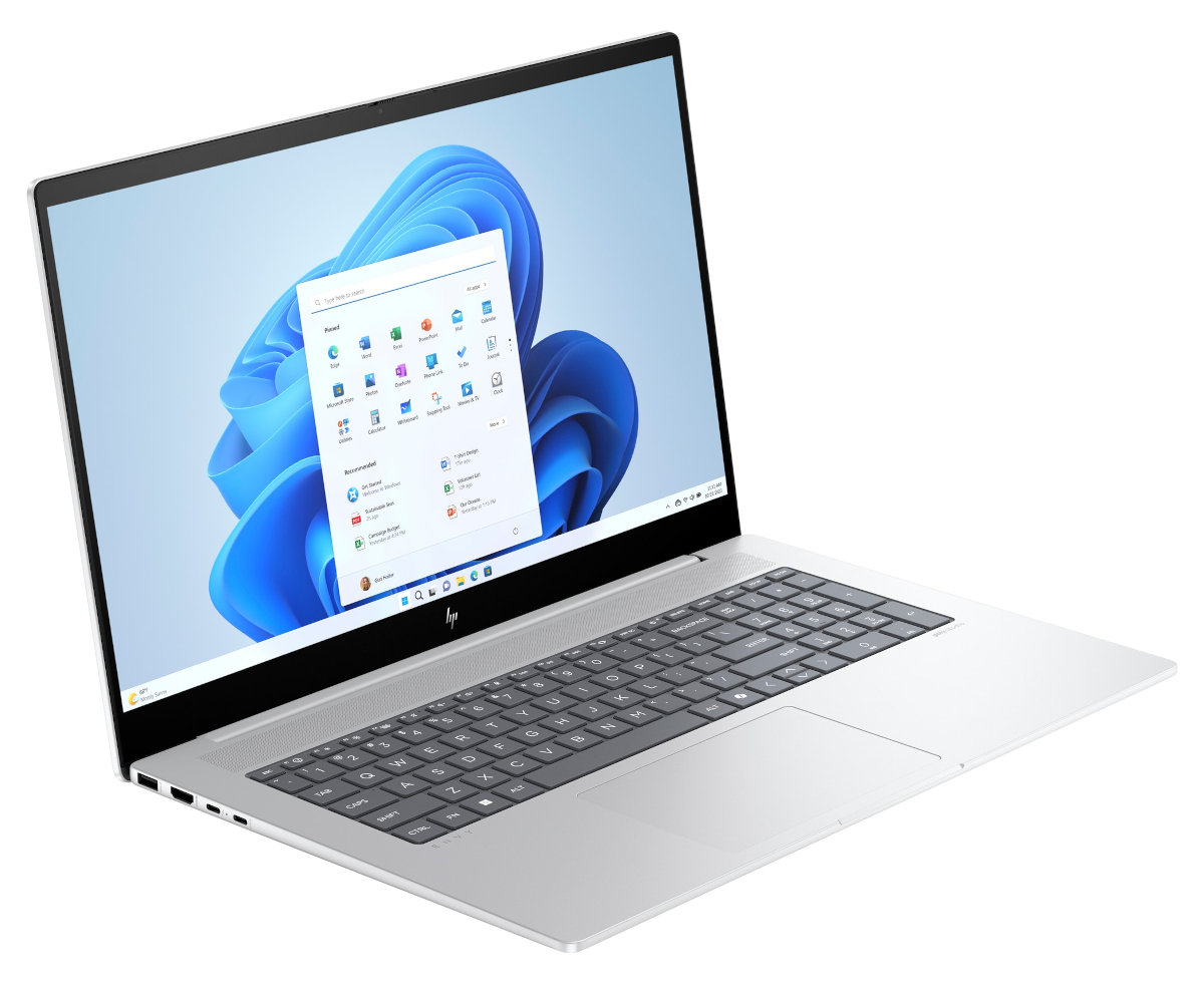 Srebrny laptop na białej powierzchni, otwarty z interfejsem Windows 11, pokazujący aplikacje i klawiaturę.