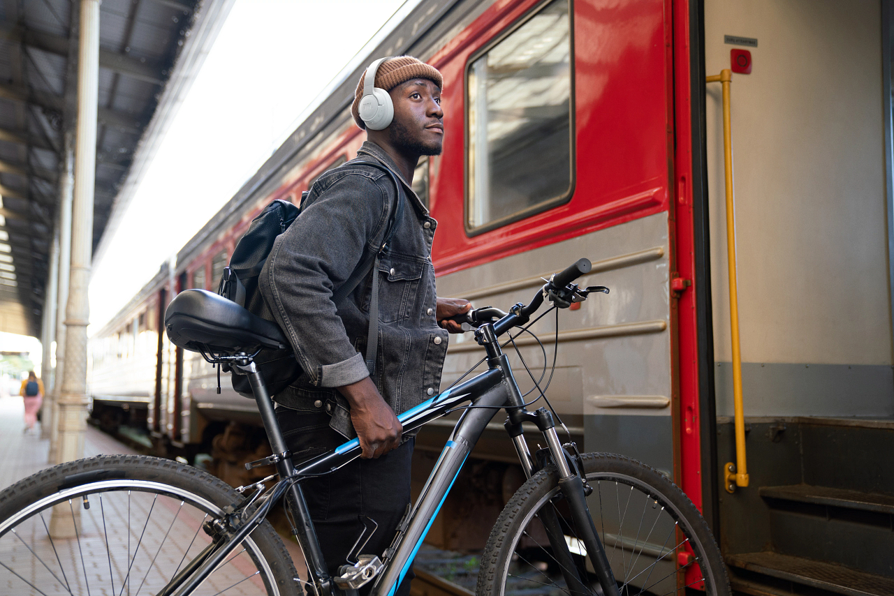 Schwarzer Mann mit Kopfhörern und Rucksack neben einem roten Zug und einem Fahrrad.