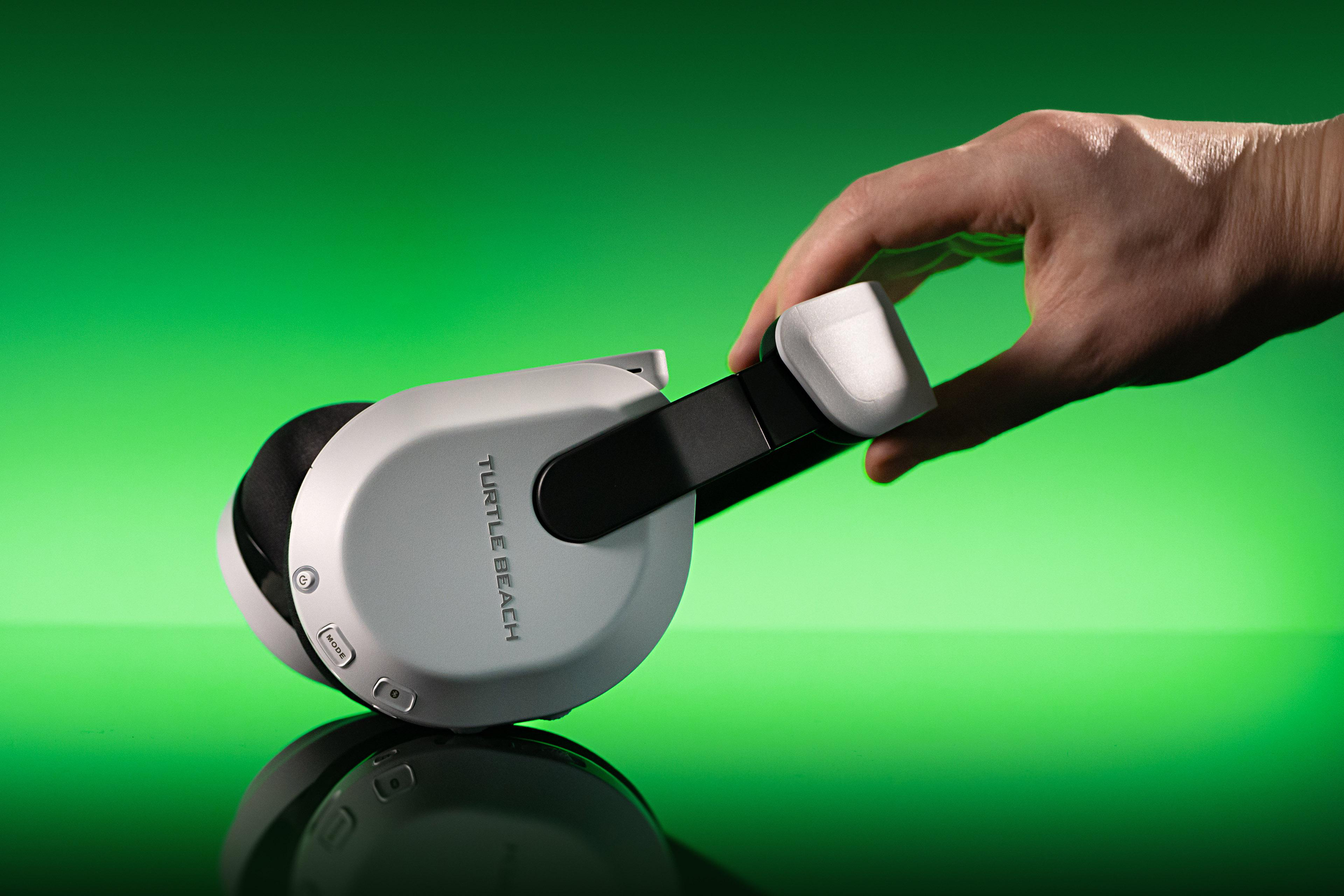 Eine Hand hält ein weißes und schwarzes Turtle Beach Gaming-Headset vor grünem Hintergrund.