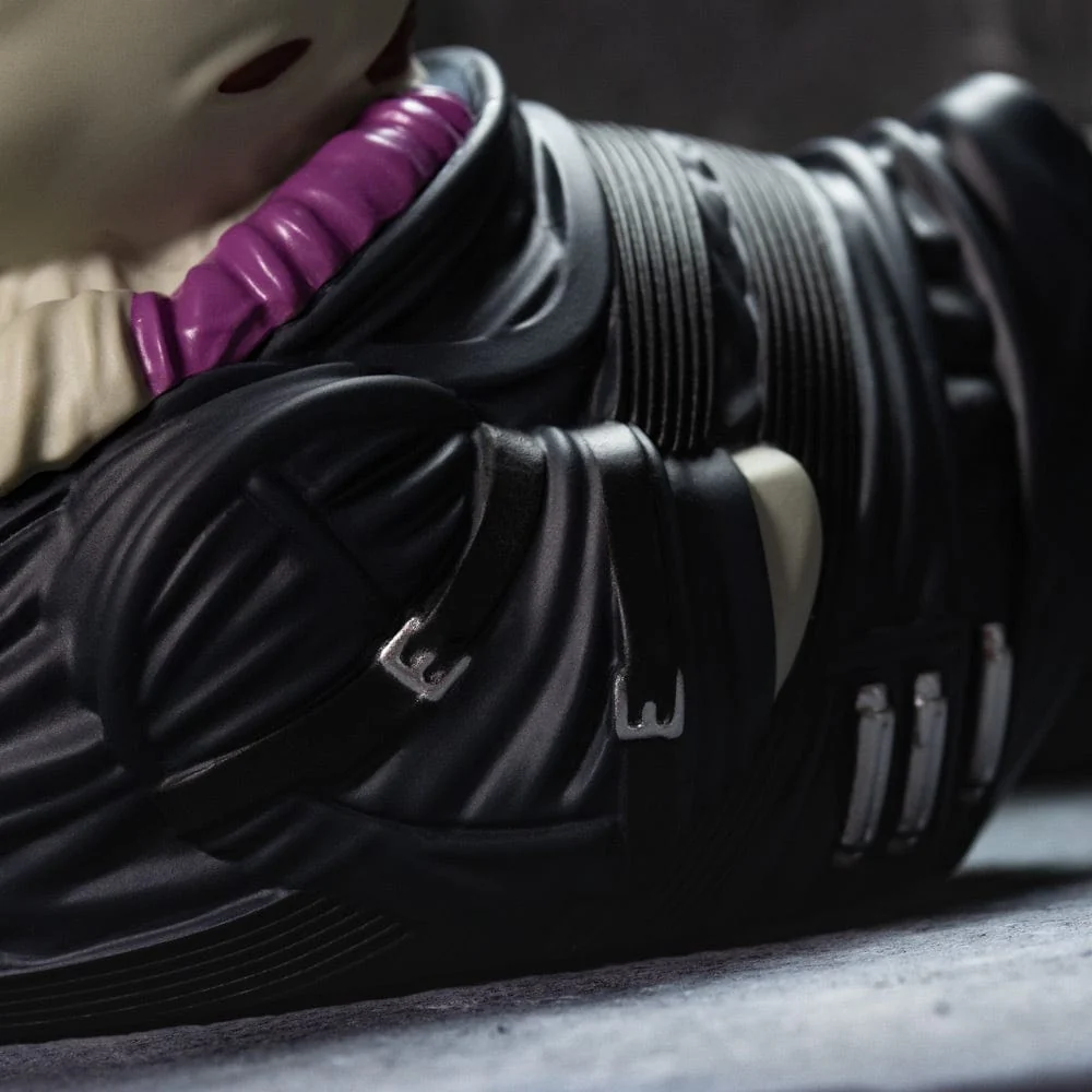 Egy fekvő figura közelképe, fekete ruhában és ezüst csatokkal.