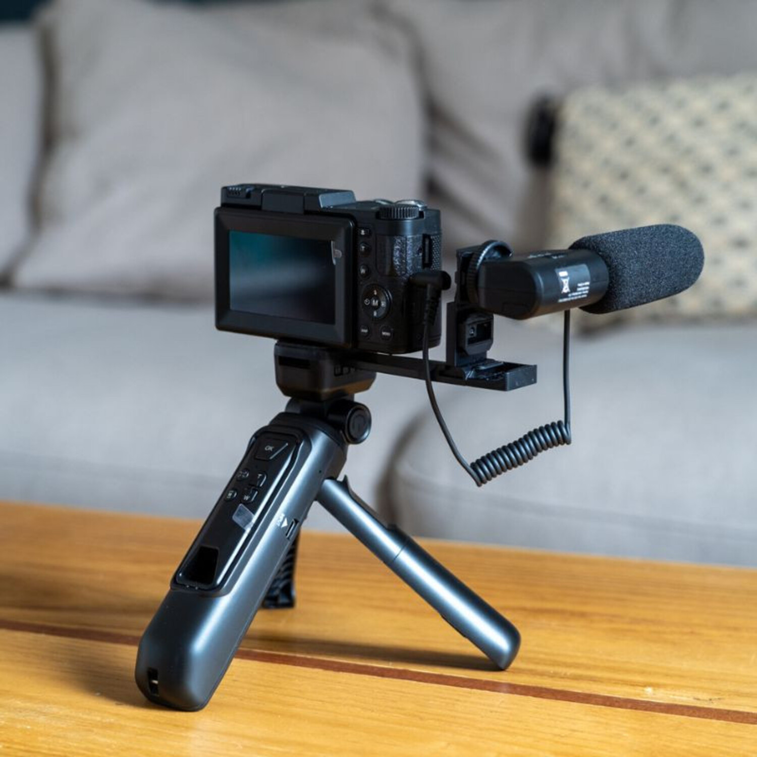 Une caméra sur un trépied avec un microphone attaché, sur une table en bois.