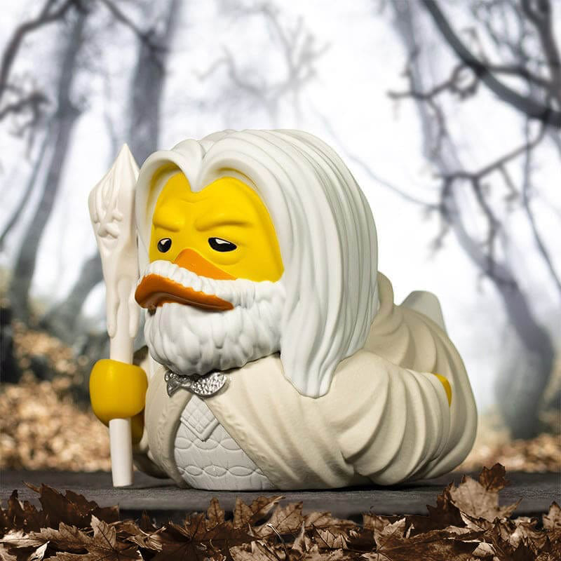 Egy Lego-szerű kacsa, Gandalfként öltözve, pálcát tartva, lehullott levelekkel borított felületen.