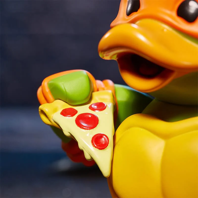 Egy Teknőc figura egy szelet pizzát tart piros pepperoni-val. Közelkép.