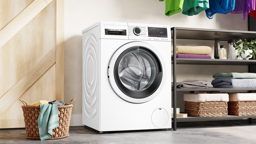Una lavadora Bosch blanca junto a una puerta de madera y un estante con toallas.