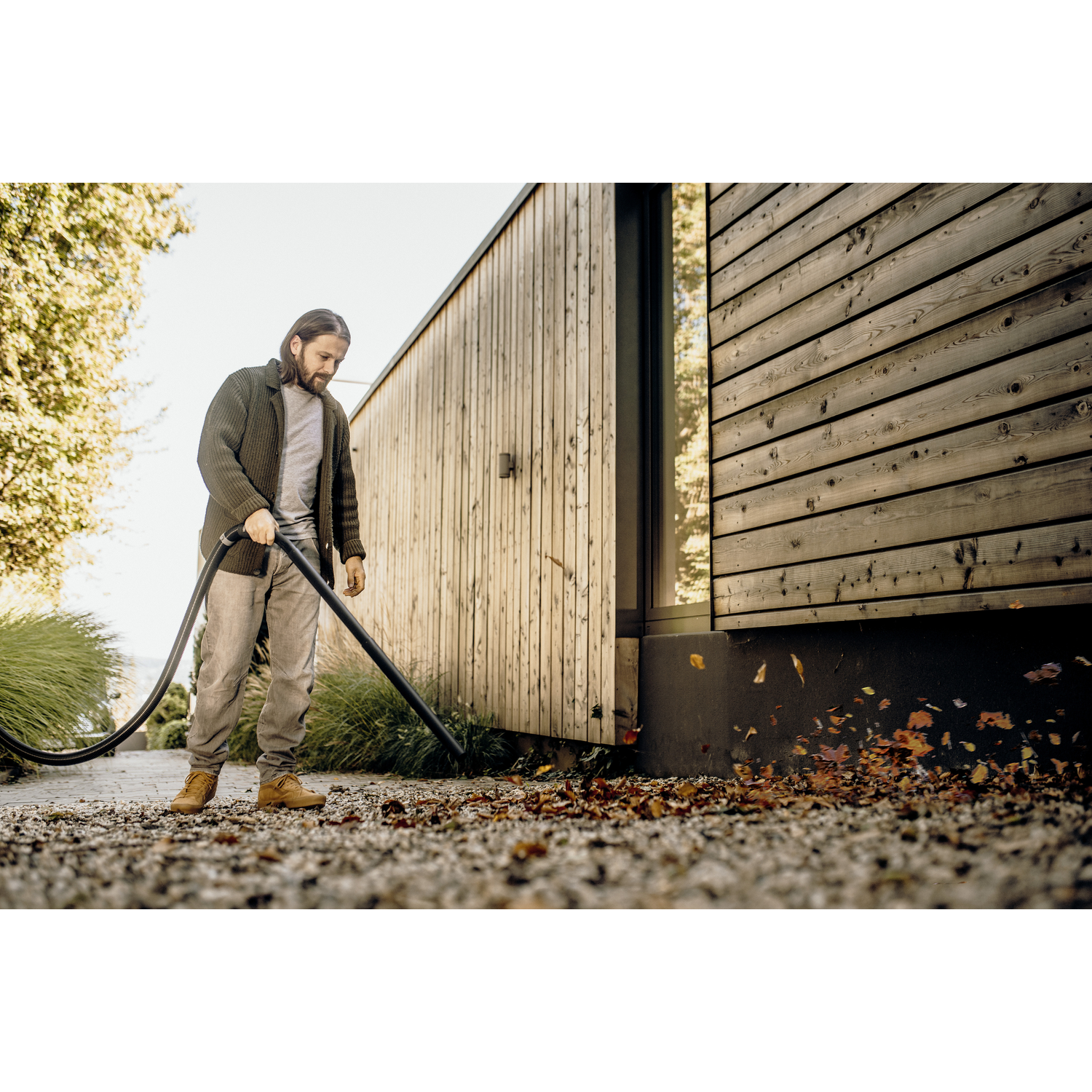 A man using a leaf vacuum to clean up leaves on a stone ground.