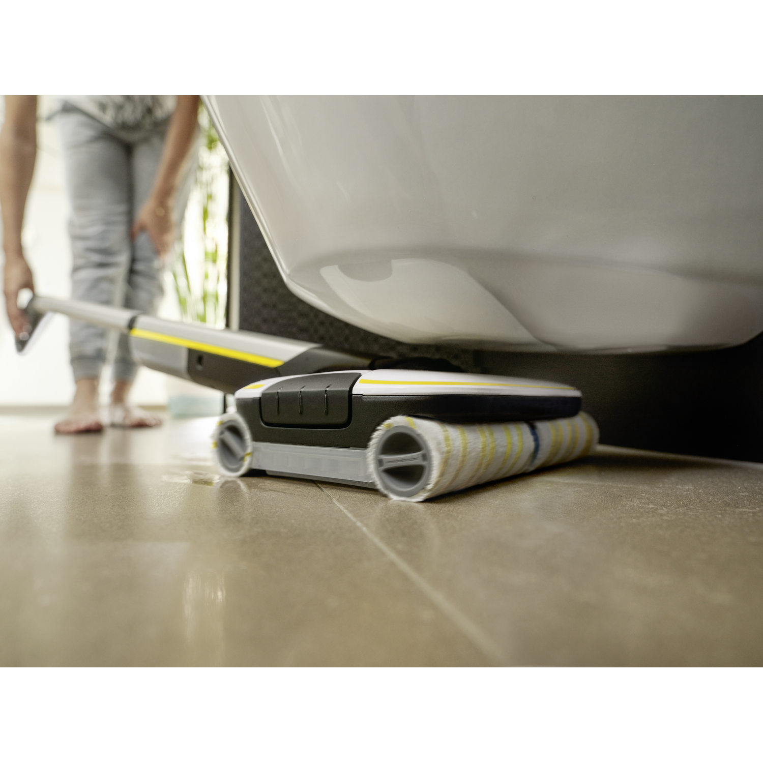 A floor cleaner under a toilet. A person is standing in background.